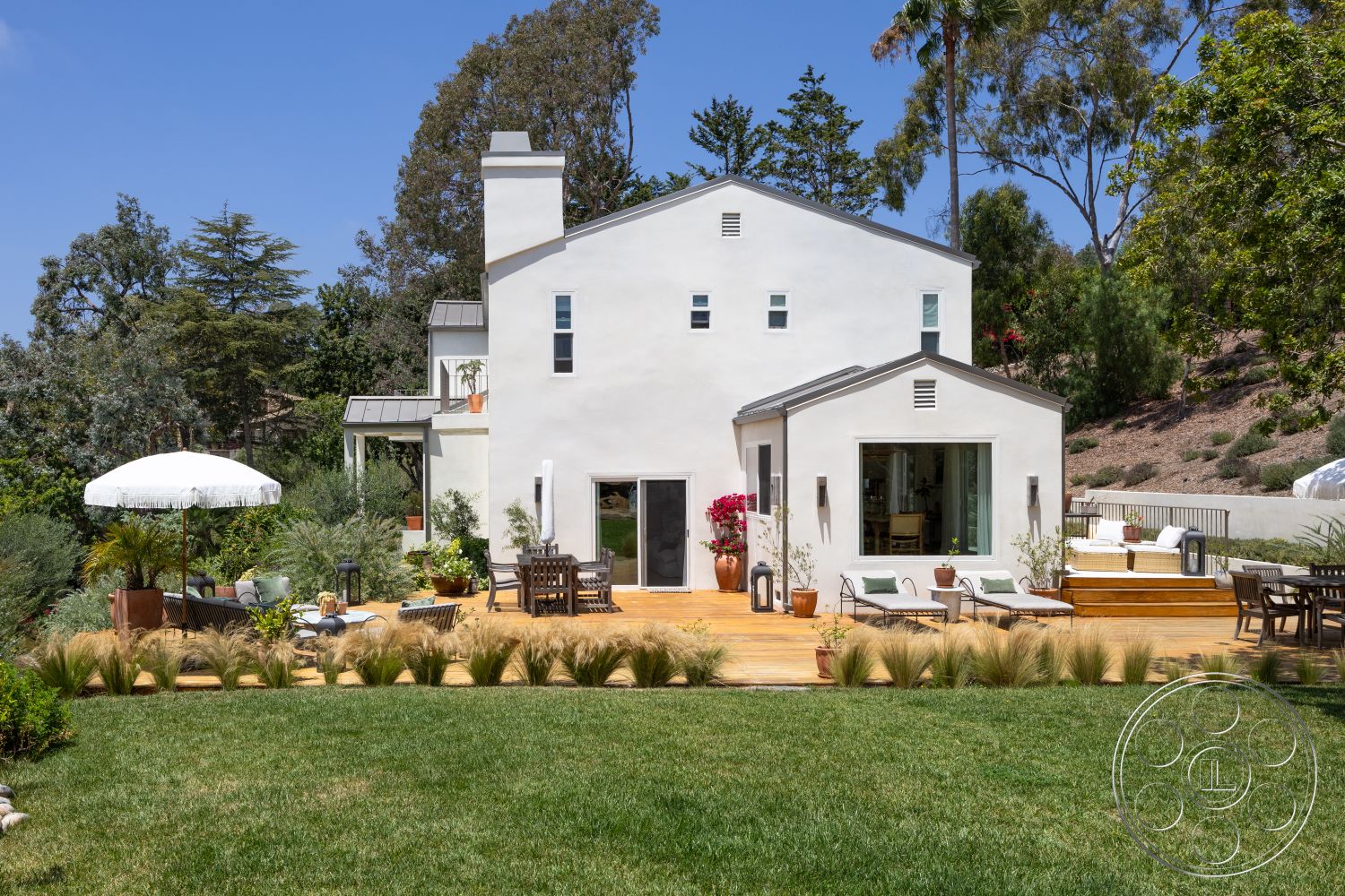 Americana 434 - exterior, landscaped garden, glass sliding doors, wooden deck, modern architectural style, gabled roof, concrete walkway, stucco walls, arched windows, outdoor lounge chairs, wooden patio furniture, terracotta planter, umbrella shade, natural grass lawn, patio dining area, foilage accents