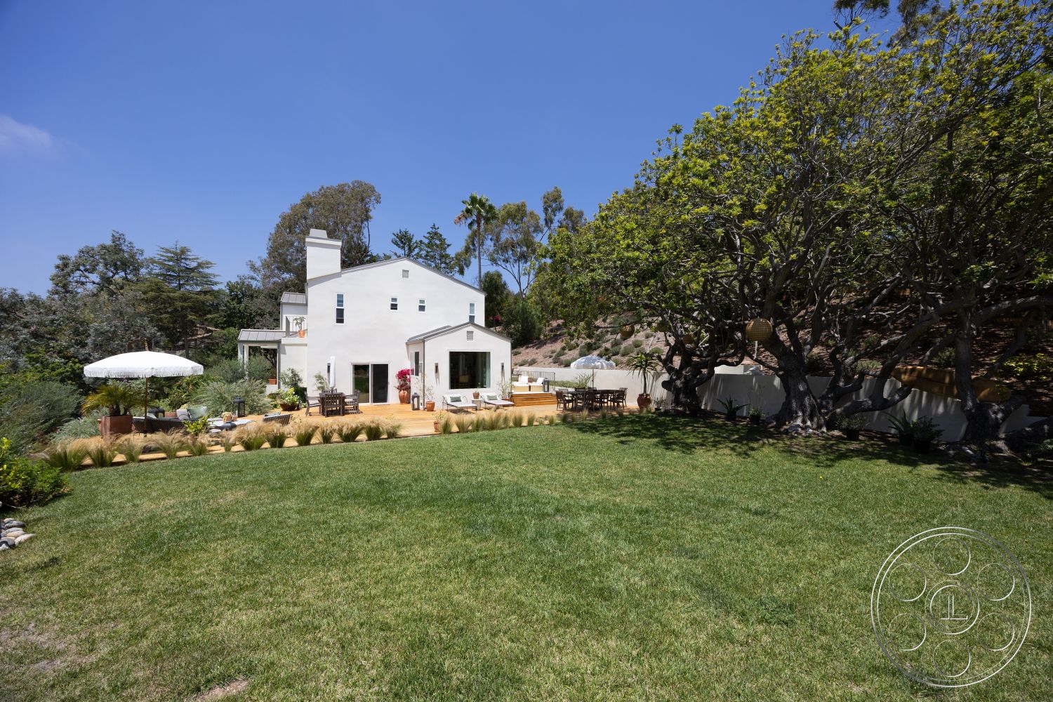 Americana 434 - large windows, exterior, flat roof, wooden deck, outdoor dining area, lawn area, mountain view, stucco walls, sun umbrella, suburban backyard, garden plants, stone landscaping, tree canopies, vaulted ceilings