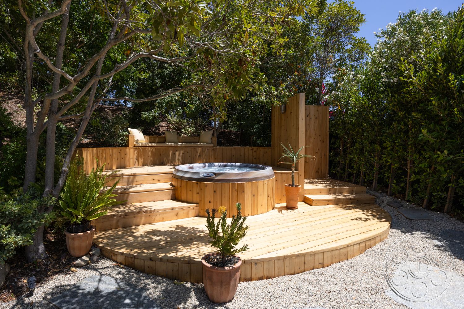 Americana 434 - exterior, surrounding greenery, natural wood decking, decorative potted plants, landscape with trees, wooden hot tub deck, circular wooden hot tub, stone accent path, terraced wood seating area, privacy wood paneling