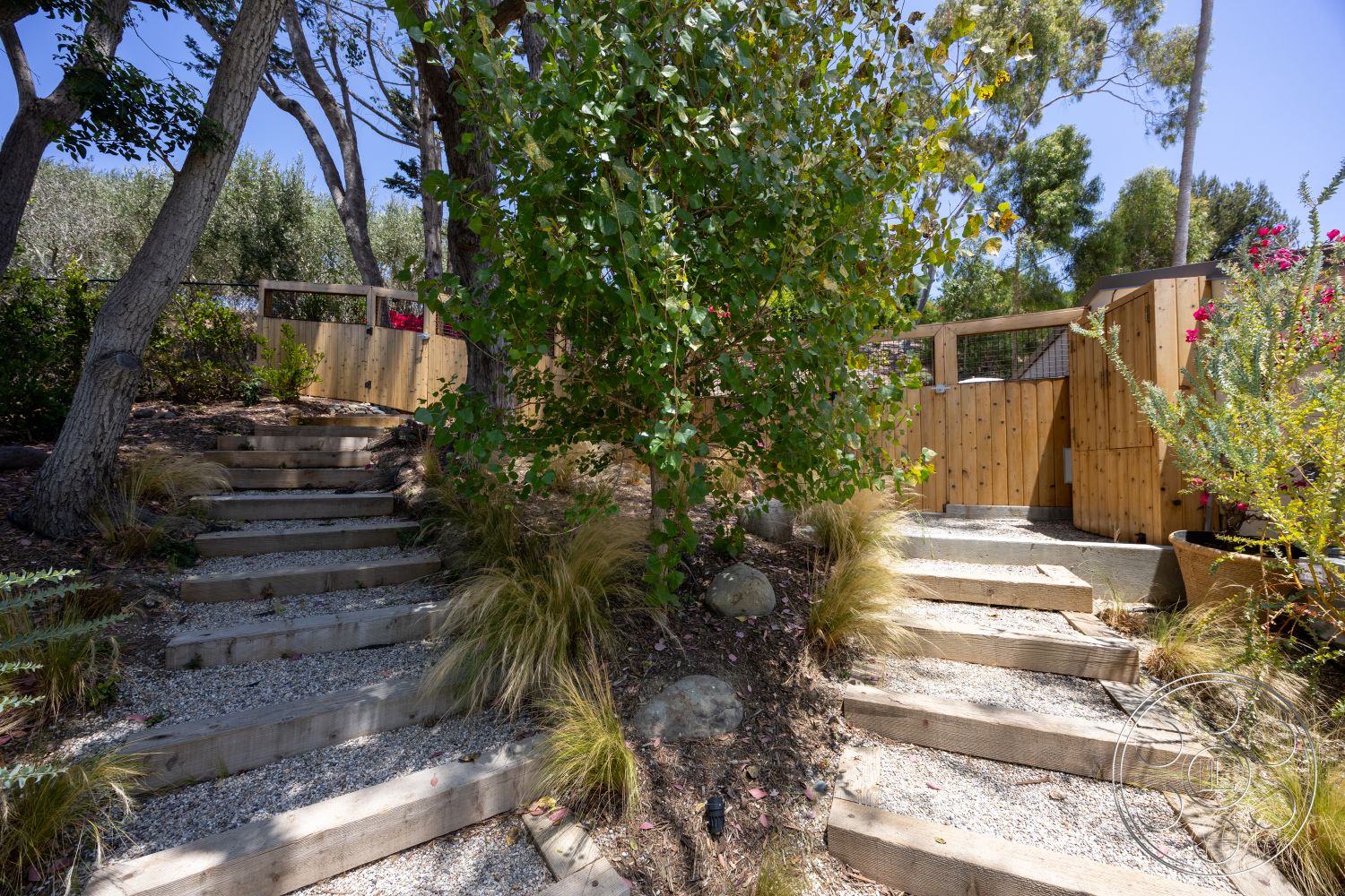 Americana 434 - exterior, natural stone accents, native plants, wooden steps, fenced garden, gravel pathway, wooden fence, tropical foliage, deciduous trees, horizontal wooden slats, landscaped garden area, decorative flower pots