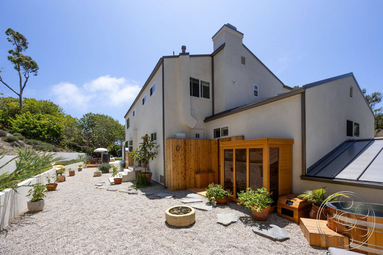 Americana 434 - outdoor seating area, natural stone pathway, decorative potted plants, lush green landscaping, wooden garden shed, stucco exterior walls, gravel patio flooring, sloped roof design, large casement windows, exterior wood siding, sunny exterior setting, wooden hot tub enclosure