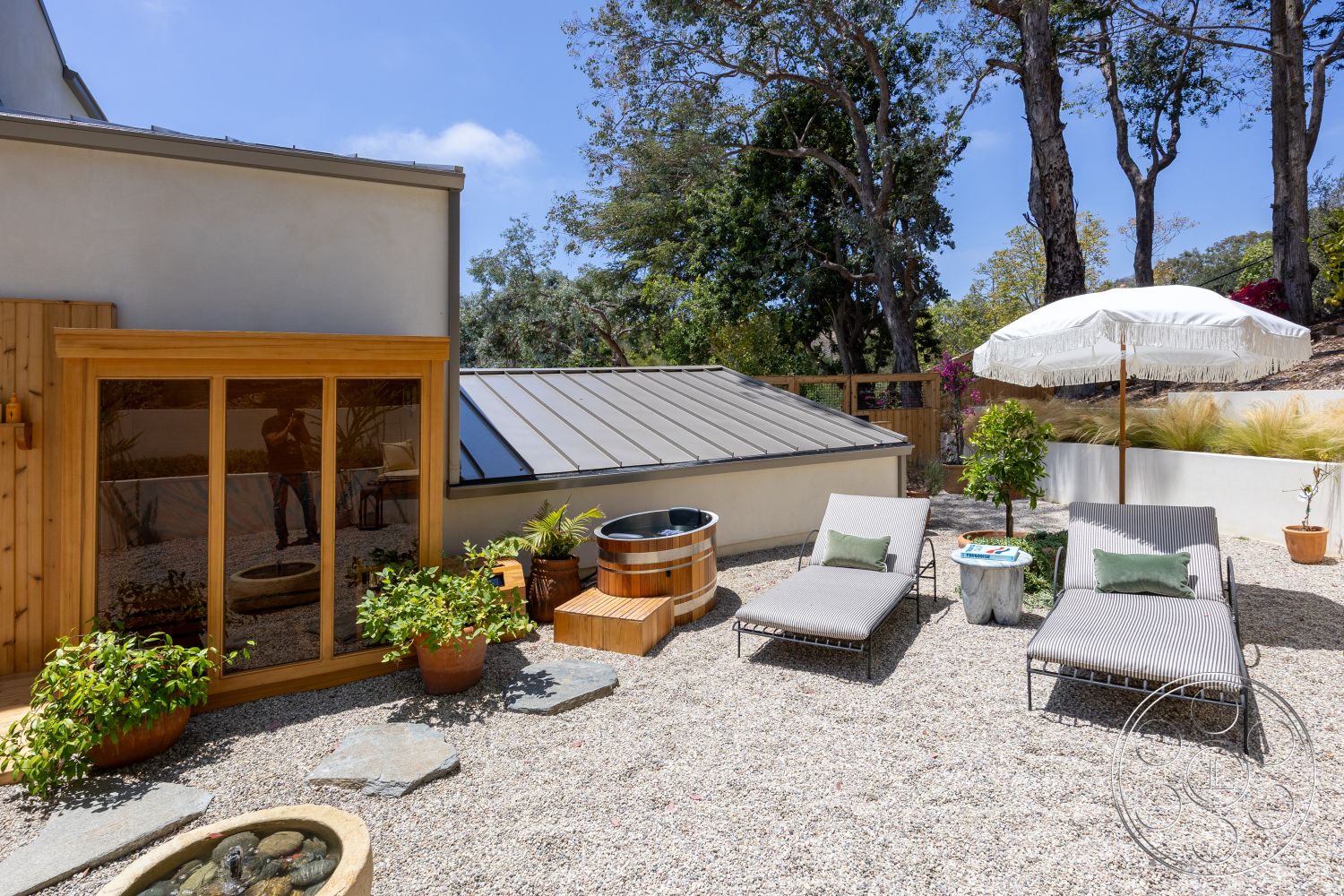 Americana 434 - exterior, contemporary home, decorative potted plants, metal roof, landscape greenery, modern lounge chairs, outdoor umbrella, natural stone patio flooring, gravel garden, wooden framed glass door, wooden spa barrel