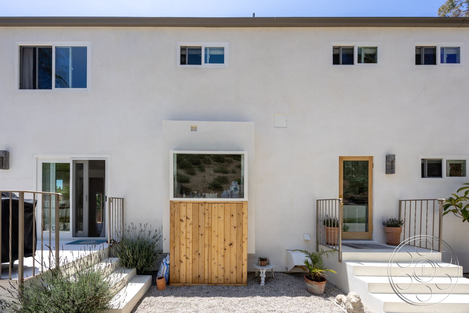 Americana 434 - exterior, large glass windows, concrete steps, stucco walls, metal balcony railings, two-story home, minimalist architectural style, landscaped gravel pathway, wooden entry gate, porch planters