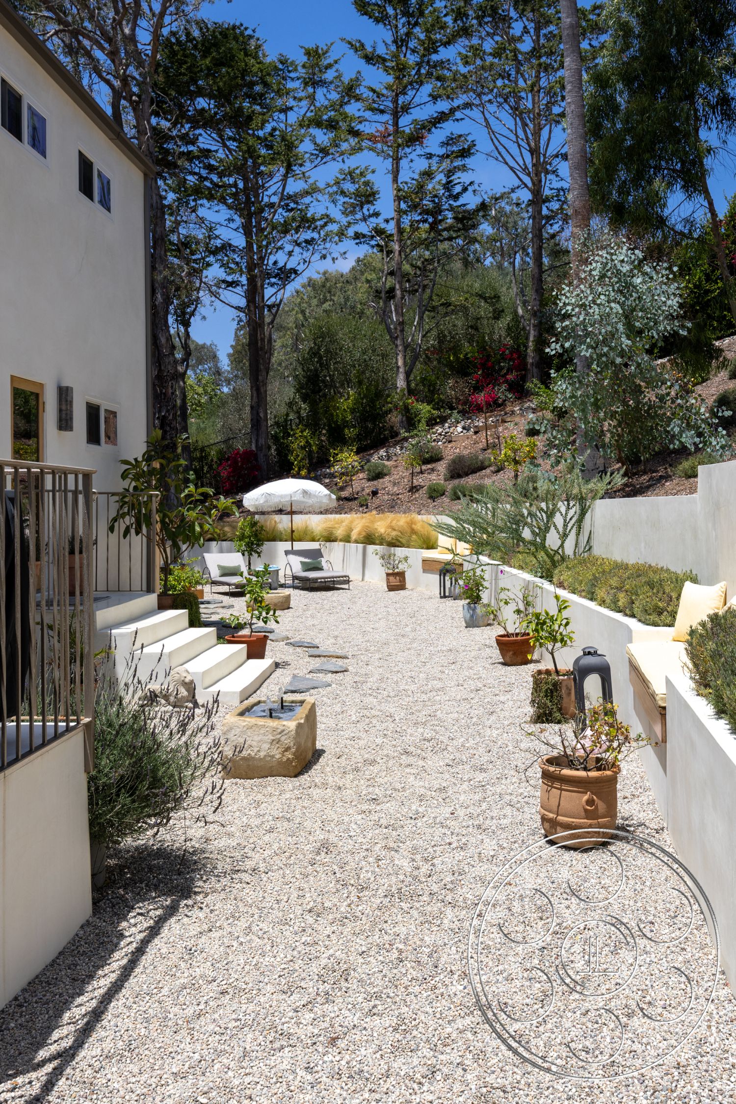 Americana 434 - exterior, floor-to-ceiling windows, concrete steps, natural stone, terracotta pots, wooden lounge chairs, outdoor umbrella, modern minimalist design, gravel patio flooring, urban garden setting, lush garden landscaping, sunny hillside location, cement wall planters, stone accent features