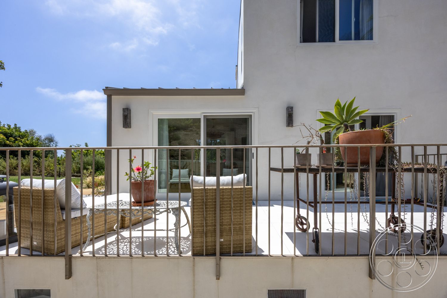 Americana 434 - exterior, glass sliding doors, natural landscaping, modern architectural style, stucco wall finish, metal railing balcony, potted succulent plants, woven outdoor seating, decorative outdoor coffee table, terra cotta planter, concrete deck surface, sloped garden area