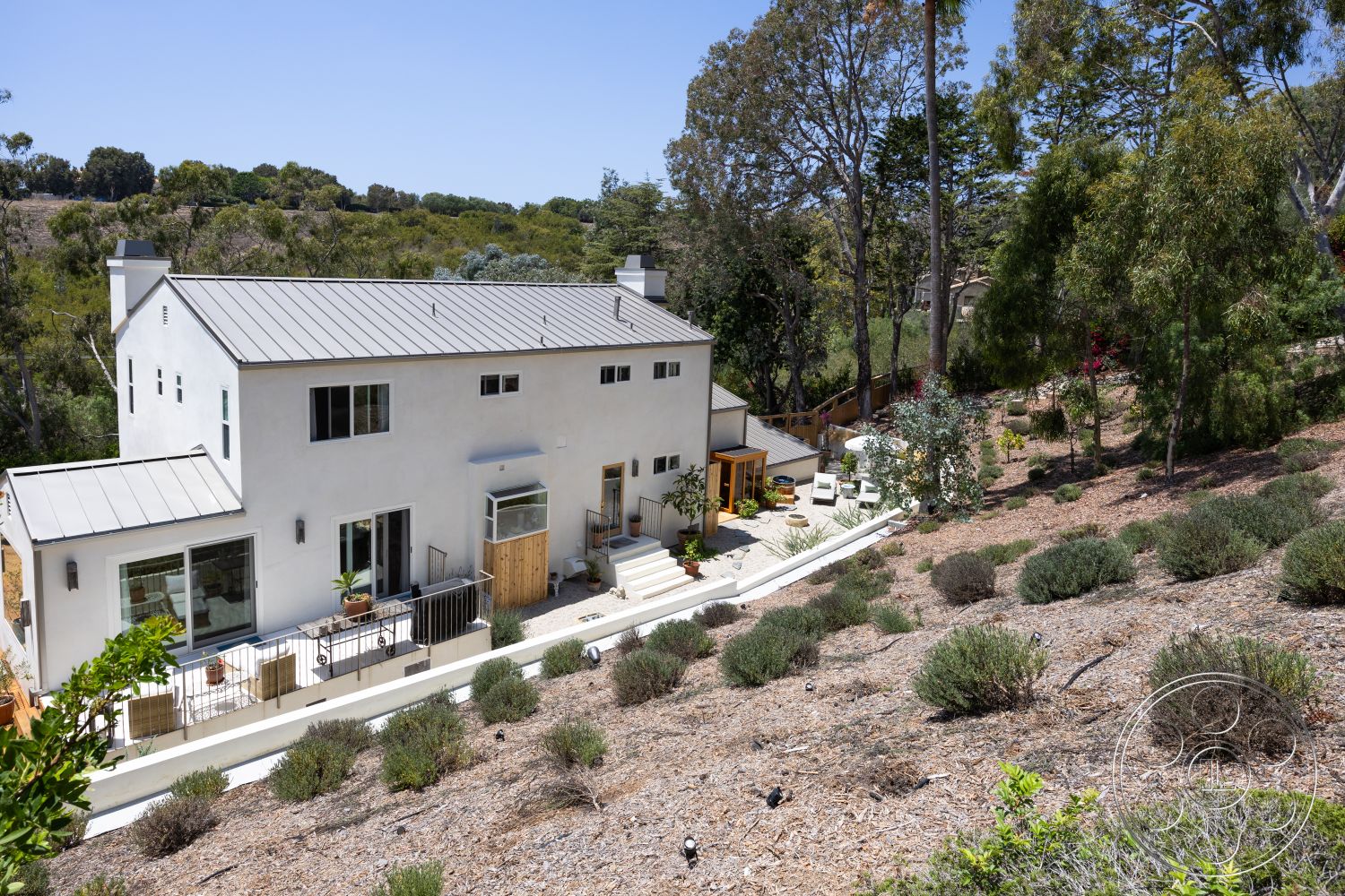 Americana 434 - exterior, sliding glass doors, outdoor seating area, natural vegetation, concrete steps, modern architectural style, landscaped hillside, metal roofing, wooden deck patio, built-in planters, green garden setting, paved patio flooring, stucco house walls, rectangle windows