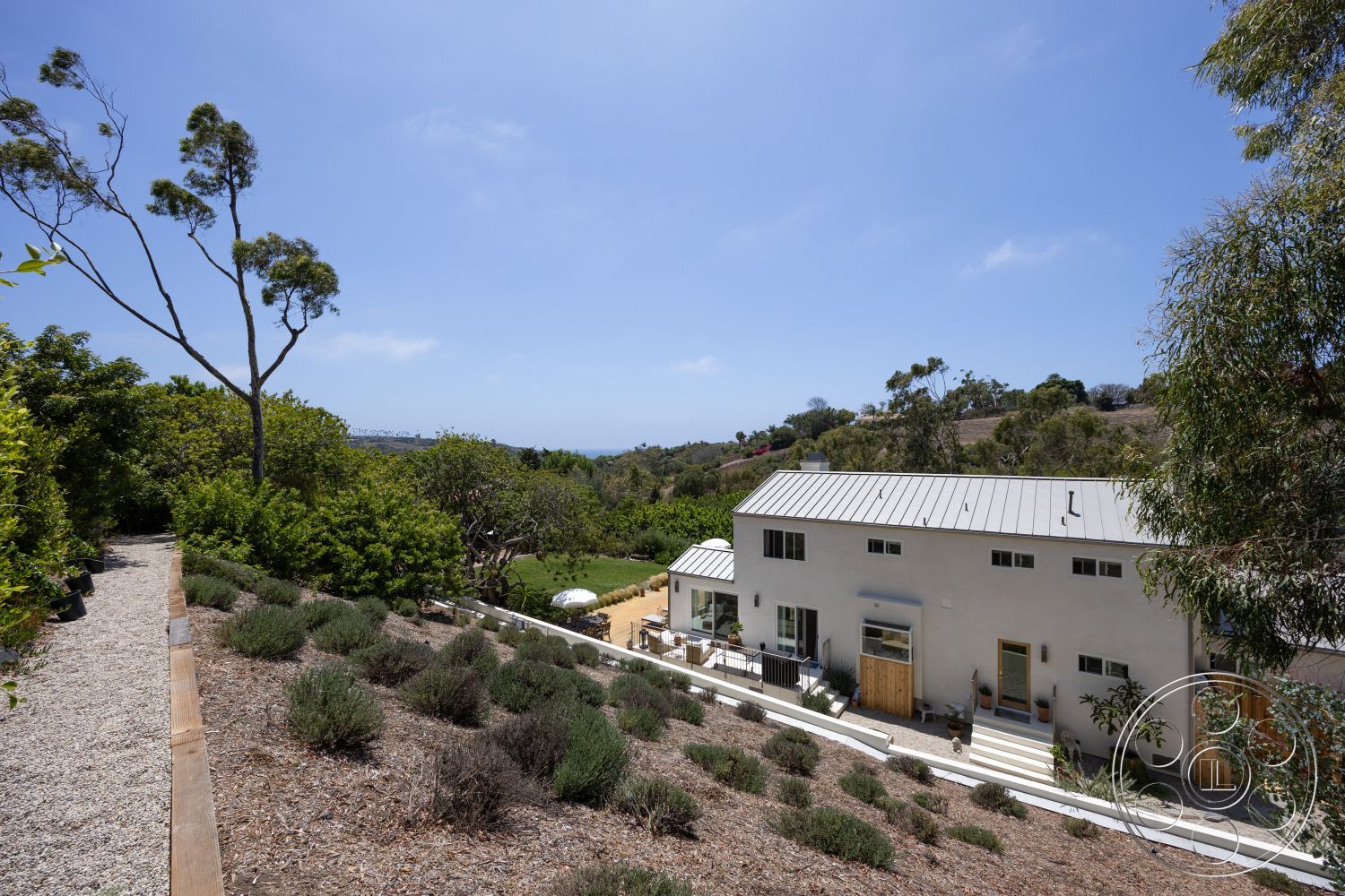 Americana 434 - exterior, wooden deck, natural vegetation, gravel pathway, stucco walls, metal roof, hillside location, landscaped garden area, modern minimalist architecture, terraced garden beds, lavender plant borders, views of surrounding landscape