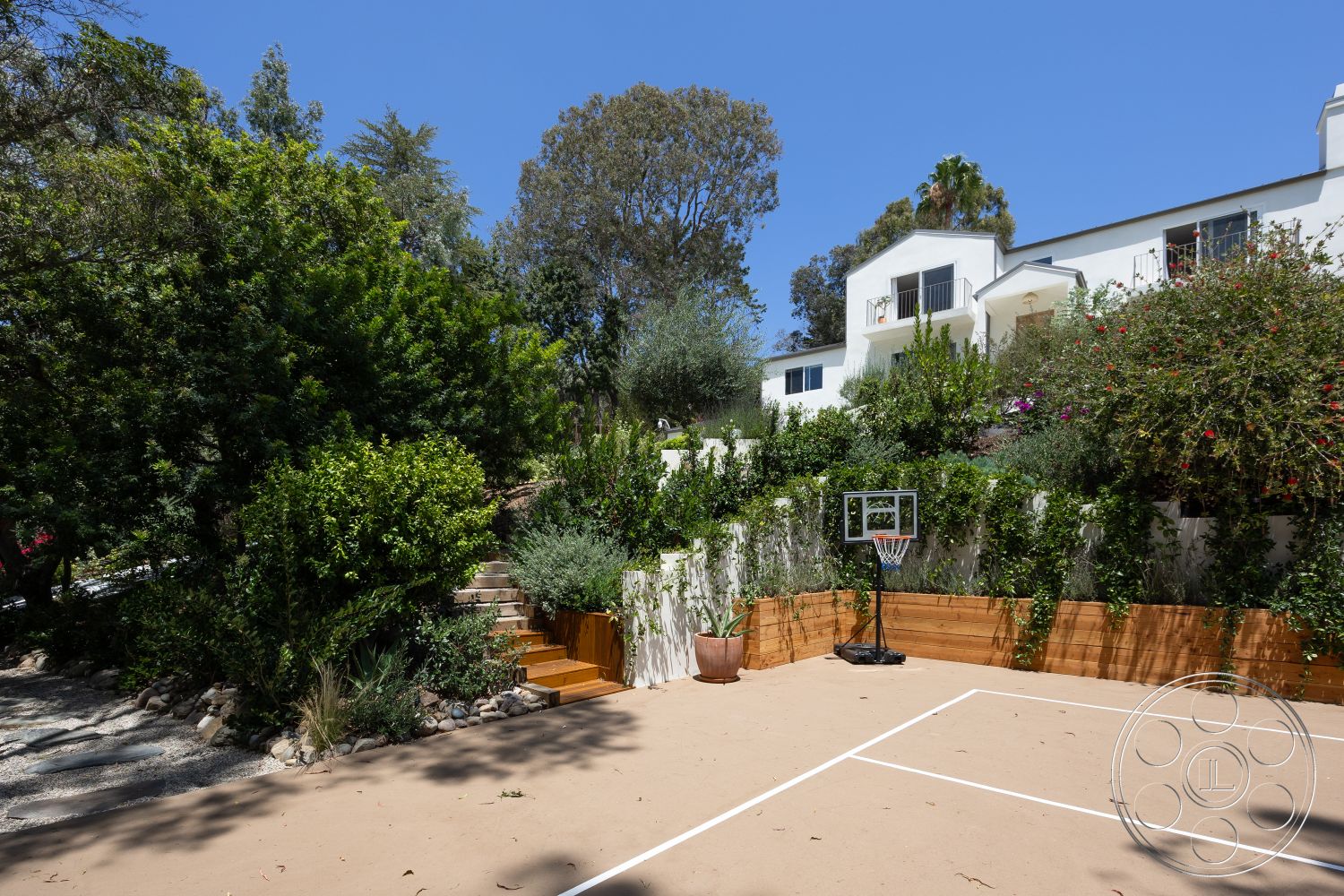Americana 434 - exterior, basketball hoop, floral accents, flat roof design, lush greenery landscaping, wooden retaining wall, two-story modern home, concrete basketball court, sand-colored surface, stone pathway steps, concrete landscaping border, slope landscape, urban outdoor area