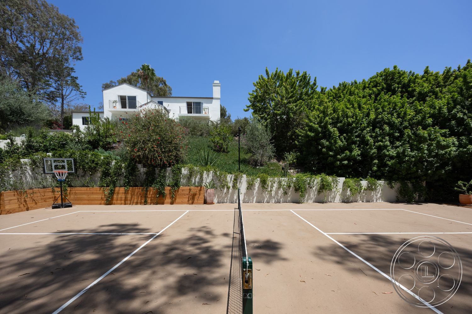 Americana 434 - exterior, landscaped garden, glass windows, clear blue sky, hillside location, lush green trees, two-story modern home, concrete tennis court, wooden perimeter fencing, brick basketball hoop