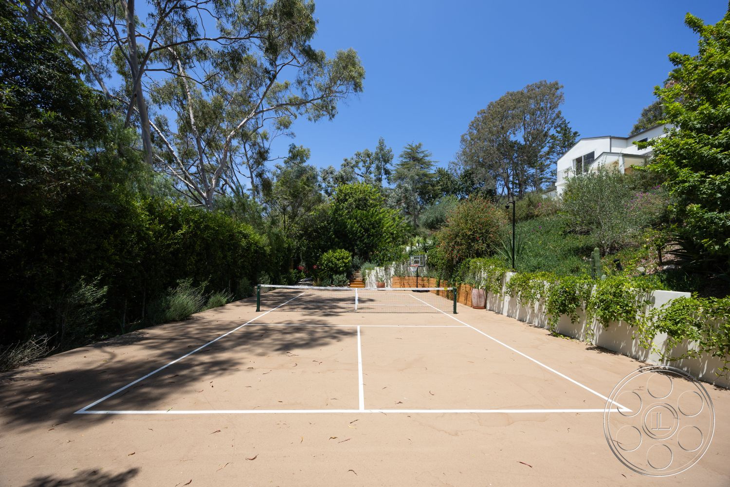 Americana 434 - exterior, surrounding greenery, residential property, mountainous backdrop, eucalyptus trees, sunny outdoor setting, sand tennis court, decorative raised garden beds, fence with climbing plants, white court lines
