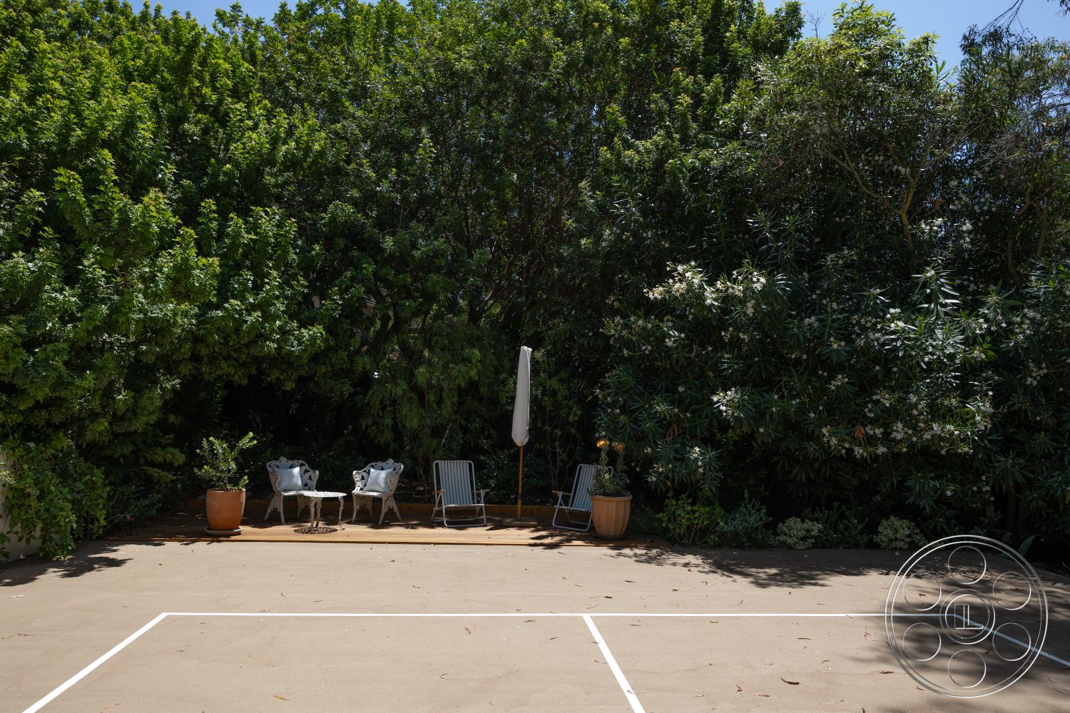 Americana 434 - exterior, decorative shrubs, white patio umbrella, concrete patio floor, rectangular outdoor seating area, green foliage landscaping, dense tree coverage, natural stone garden planters, metal frame lounge chairs, small round outdoor coffee table, clay flower pots