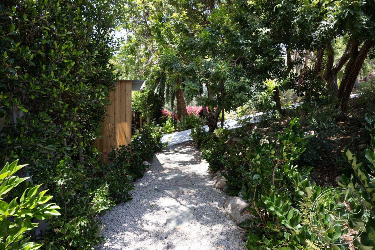Americana 434 - exterior, lush greenery, natural landscape, gravel pathway, flowering shrubs, tall trees, garden setting, wooden fence