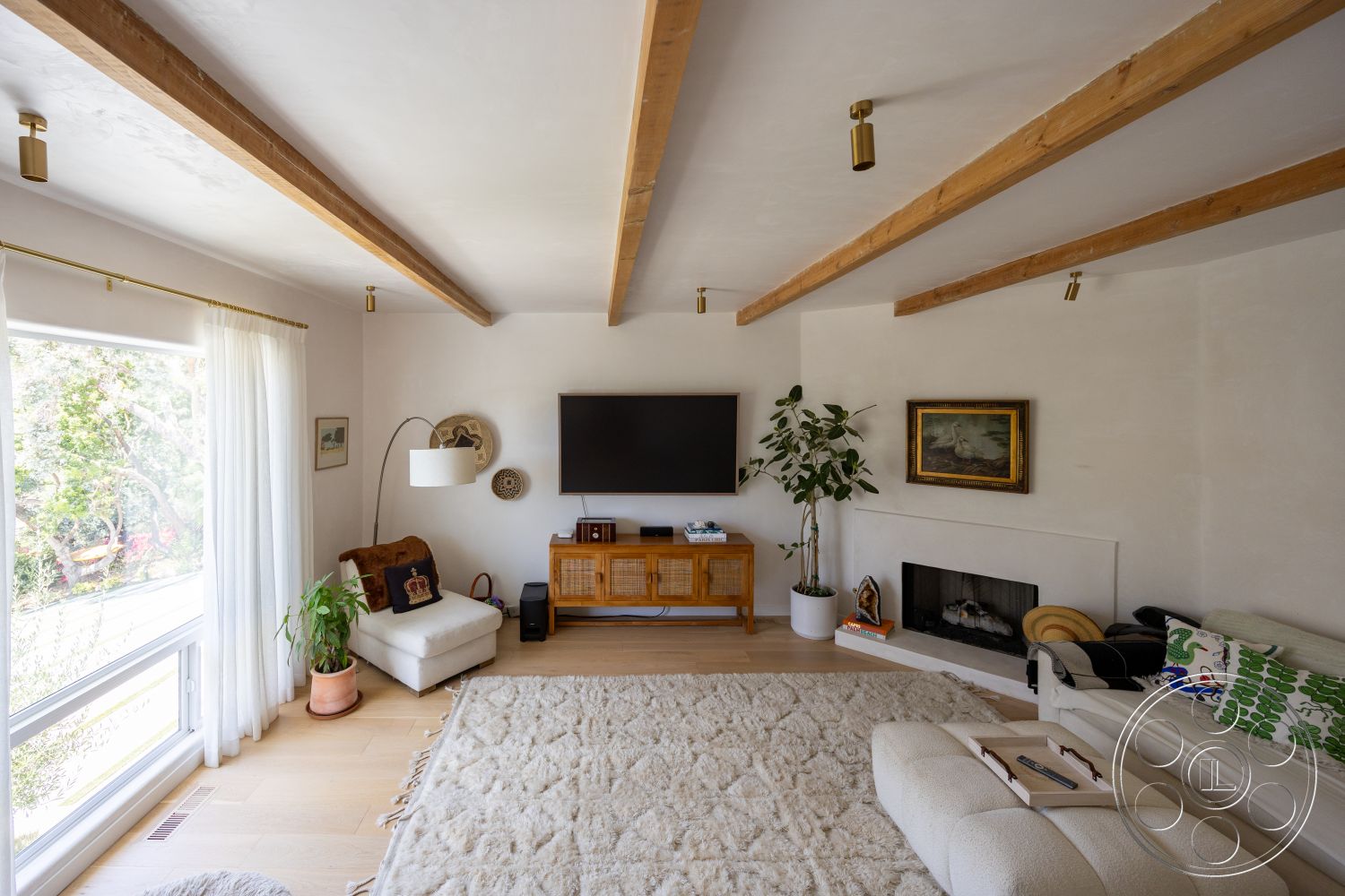 Americana 434 - light hardwood flooring, minimalist furniture, floor-to-ceiling windows, contemporary armchair, wood beam ceiling, modern entertainment center, white textured plaster walls, plant accent, fabric area rug, fireplace with clean lines, soft textile curtains, artwork framed in gold