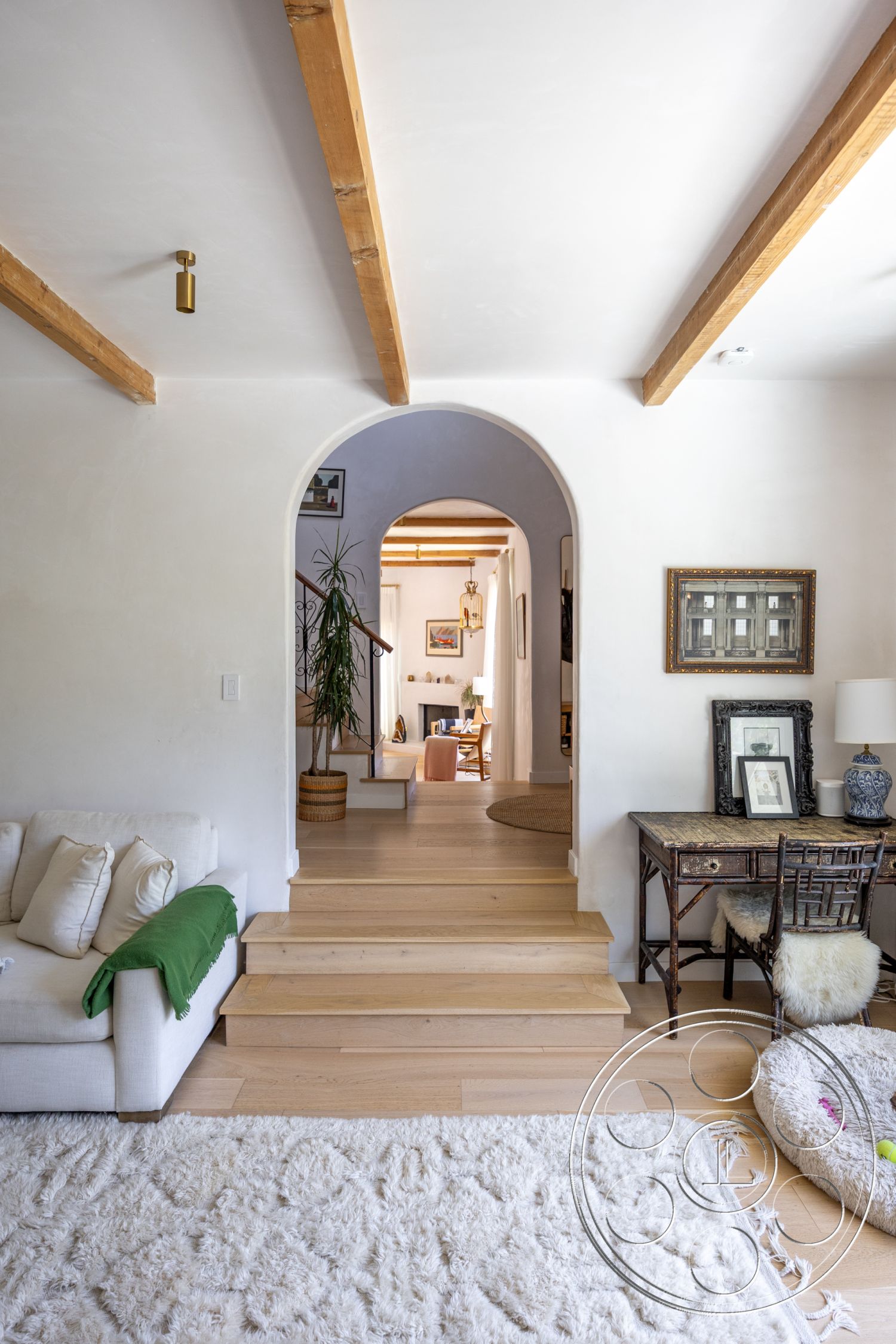 Americana 434 - natural light, indoor plant, light hardwood flooring, dining area, framed artwork, arched doorway, ambient lighting fixtures, exposed wood ceiling beams, smooth plaster walls, decorative side table, soft woven area rug, neutral sofa with throw pillows, stepped wooden staircase