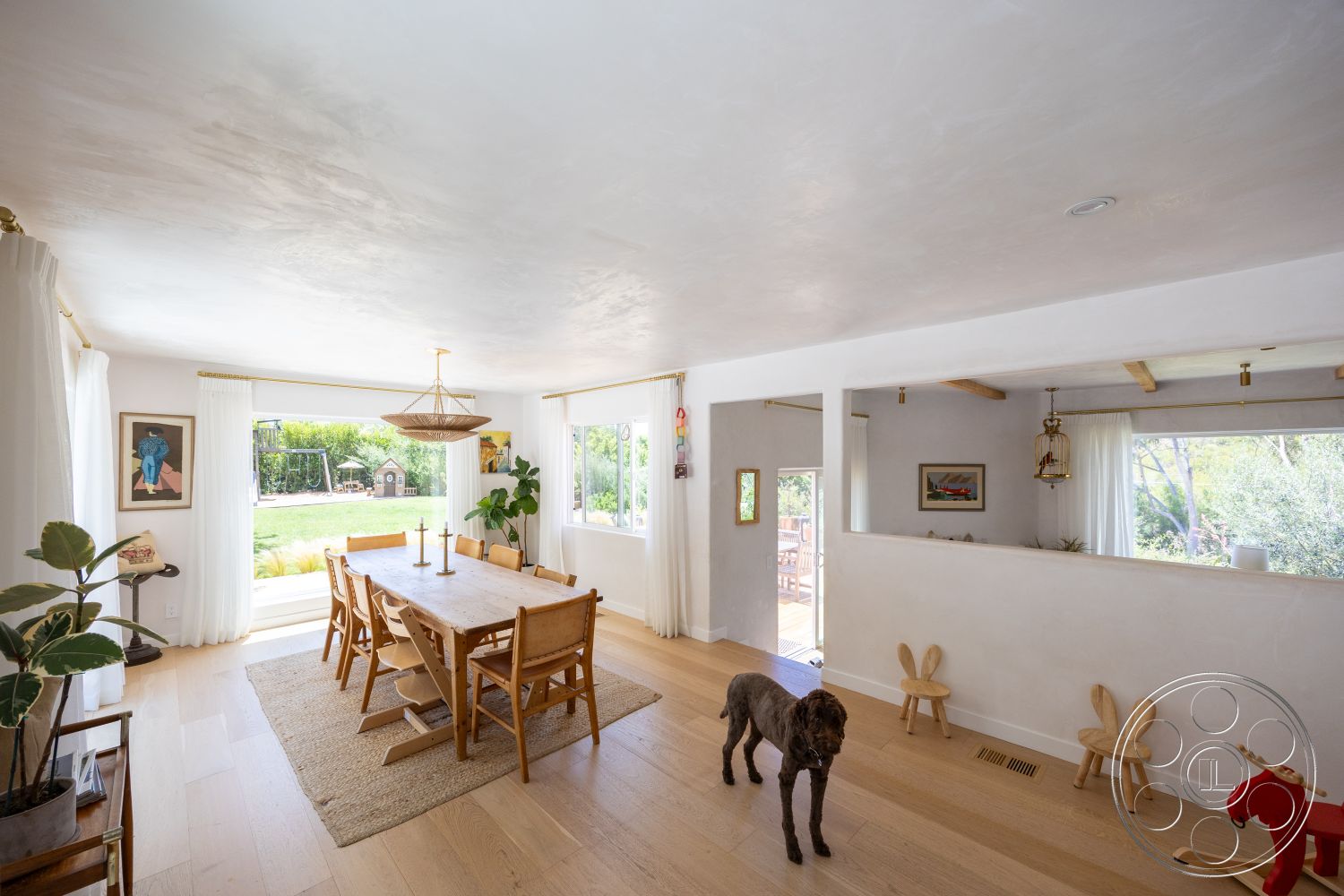 Americana 434 - neutral color palette, natural light, dining room, plant decor, open floor plan, wood dining table, floor-to-ceiling windows, hardwood floor, textured plaster ceiling, woven area rug, modern minimalist decor, view of garden, glass sliding door, white painted walls, exposed wood ceiling beam, curtains with curtain rod