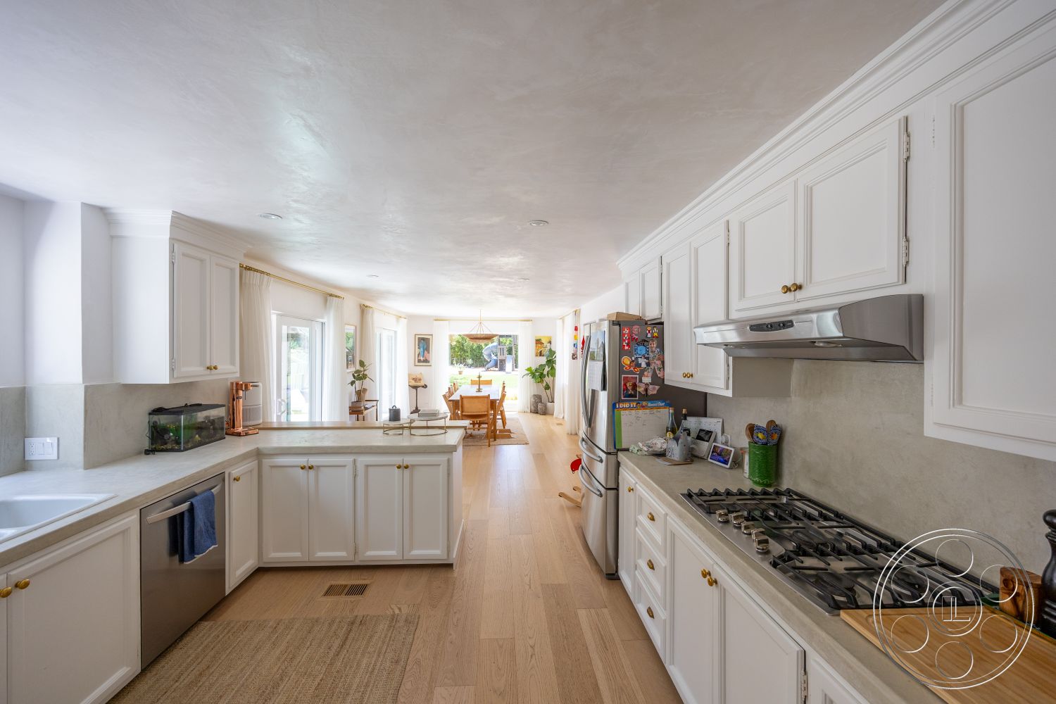 Americana 434 - floor-to-ceiling windows, modern decor accents, textured plaster ceiling, stainless steel refrigerator, open dining area, natural light-filled space, stainless steel gas range, light wood plank flooring, concrete kitchen countertops, kitchen island with seating, white shaker-style kitchen cabinets, bronze kitchen faucet