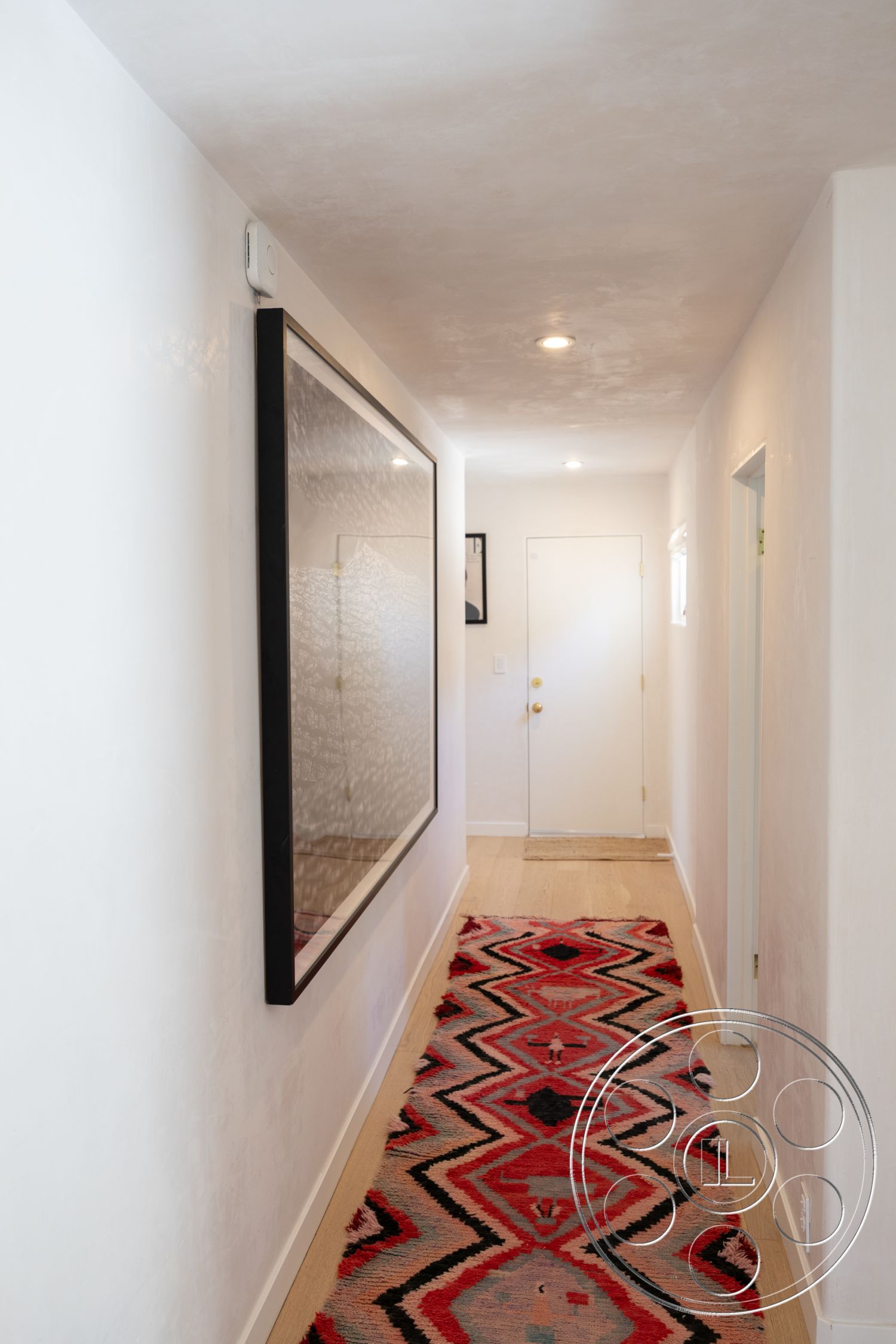 Americana 434 - exterior, textured plaster walls, recessed ceiling lights, modern door design, white painted interior walls, geometric patterned area rug, large framed mirror, natural wood plank flooring