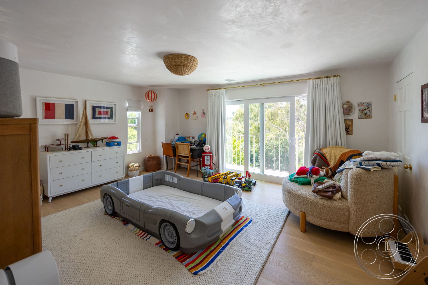 Americana 434 - natural light, hardwood flooring, sliding glass doors, family-friendly design, woven area rug, child's play area, colorful wall decor, wood dresser, woven pendant light fixture, white painted walls, tufted boucle armchair, car-themed bed frame, modern children's room