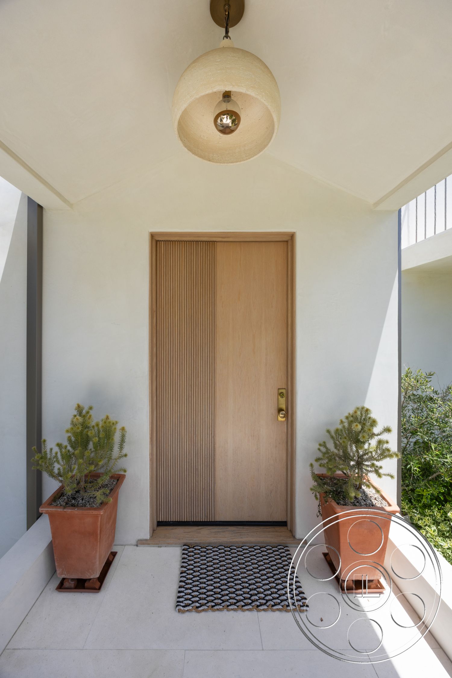 Americana 434 - exterior, terracotta planters, textured plaster walls, succulent plants, wood front door, suspended light fixture, concrete porch flooring, vertical wood paneling door, woven doormat
