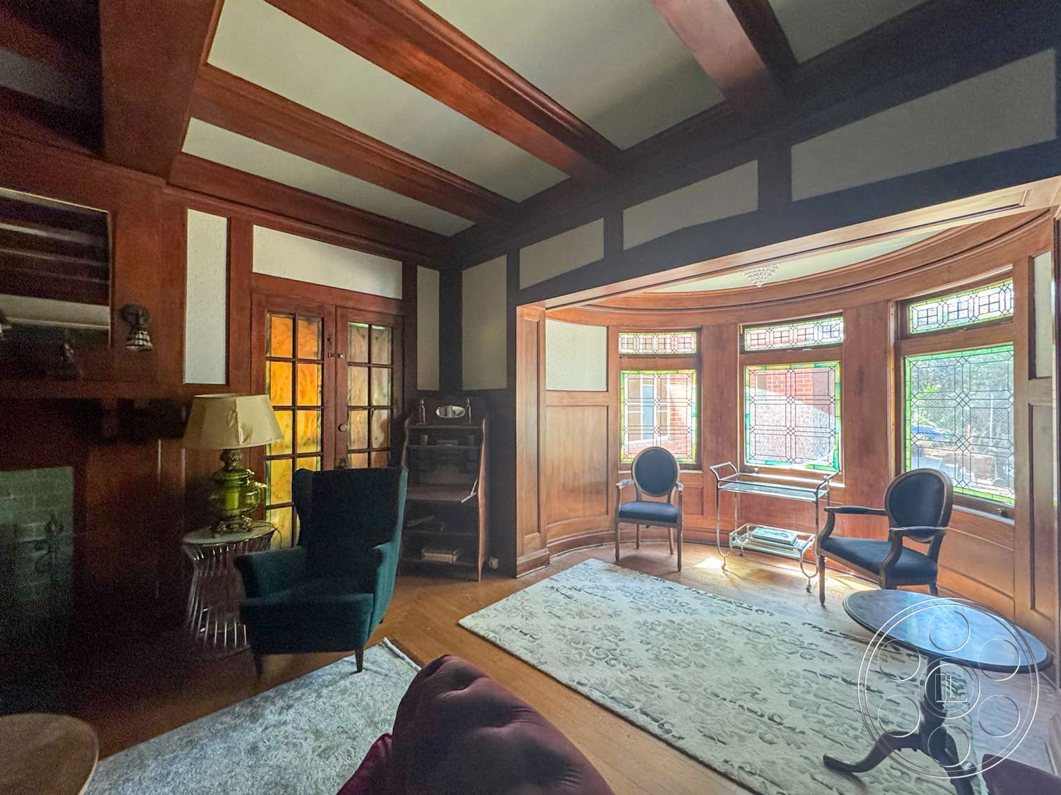 The Rosenheim Mansion - hardwood flooring, stained glass windows, dark wood paneling, craftsman architectural style, built-in cabinetry, decorative table lamp, oriental area rug, wood beam ceiling, curved bay window, traditional armchairs