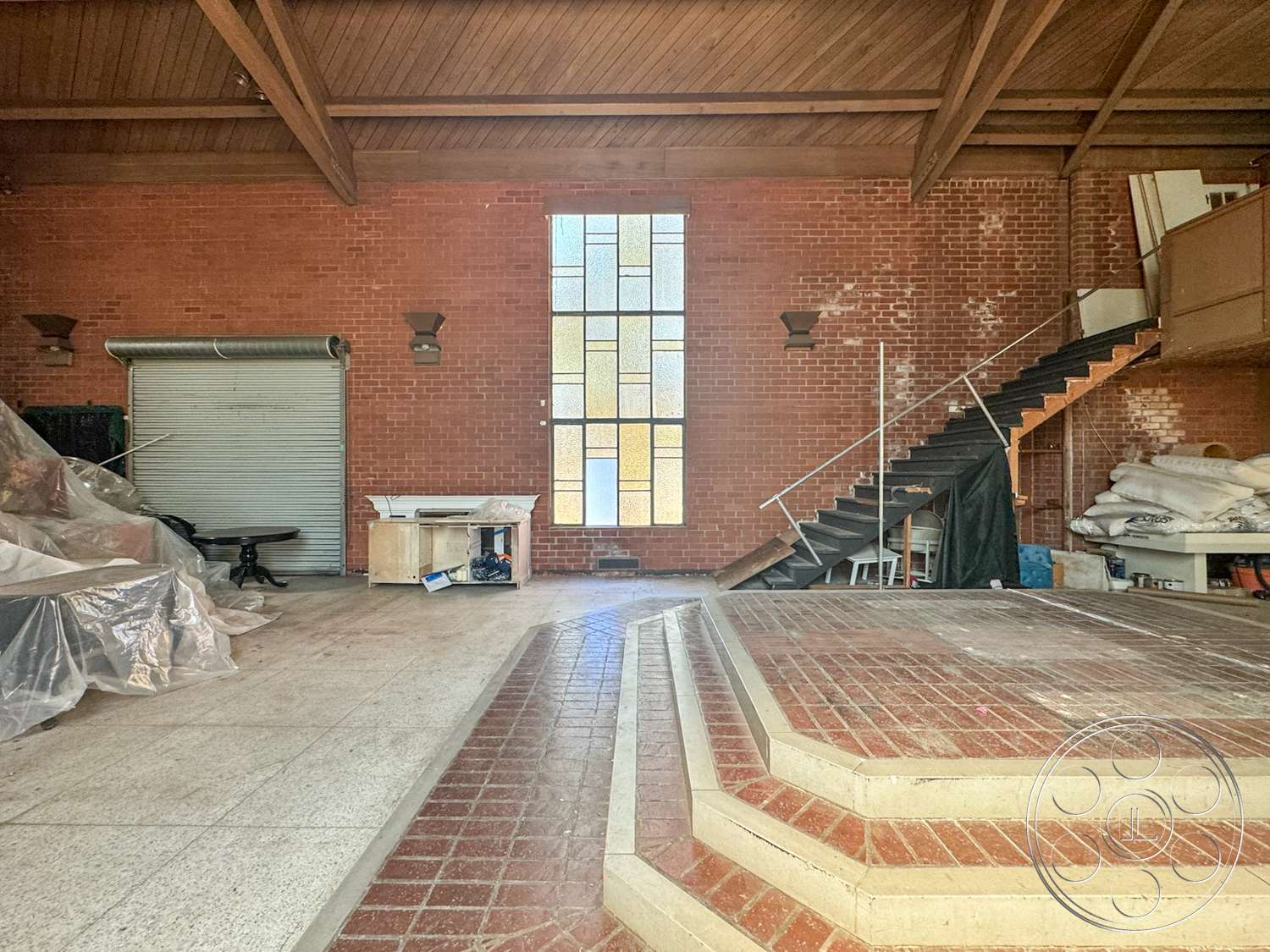 The Rosenheim Mansion - exposed brick walls, brick flooring, stained glass window, built-in cabinetry, open-plan layout, wood beam ceiling, metal stair railings, curved concrete steps, industrial roller door