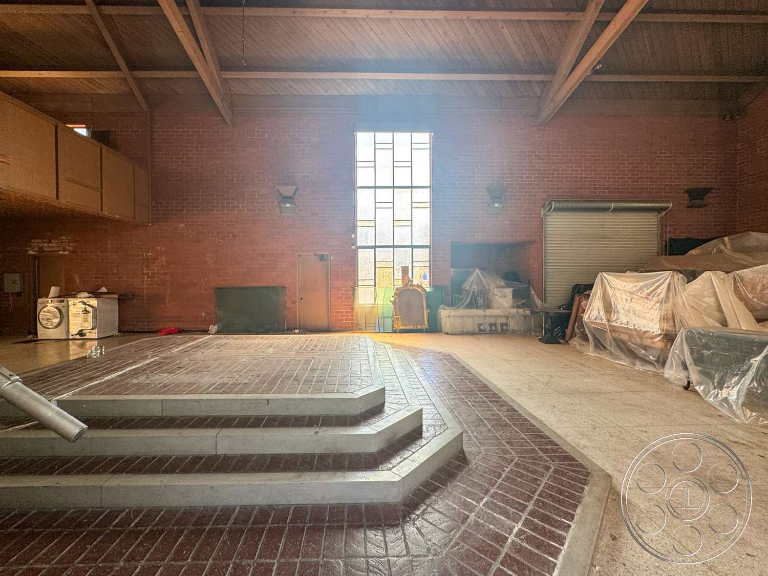 The Rosenheim Mansion - industrial style, exposed brick walls, red brick flooring, wood beam ceiling, staircase with concrete steps, large stained glass window, indoor lighting sconces, unfinished open space, low ceiling height