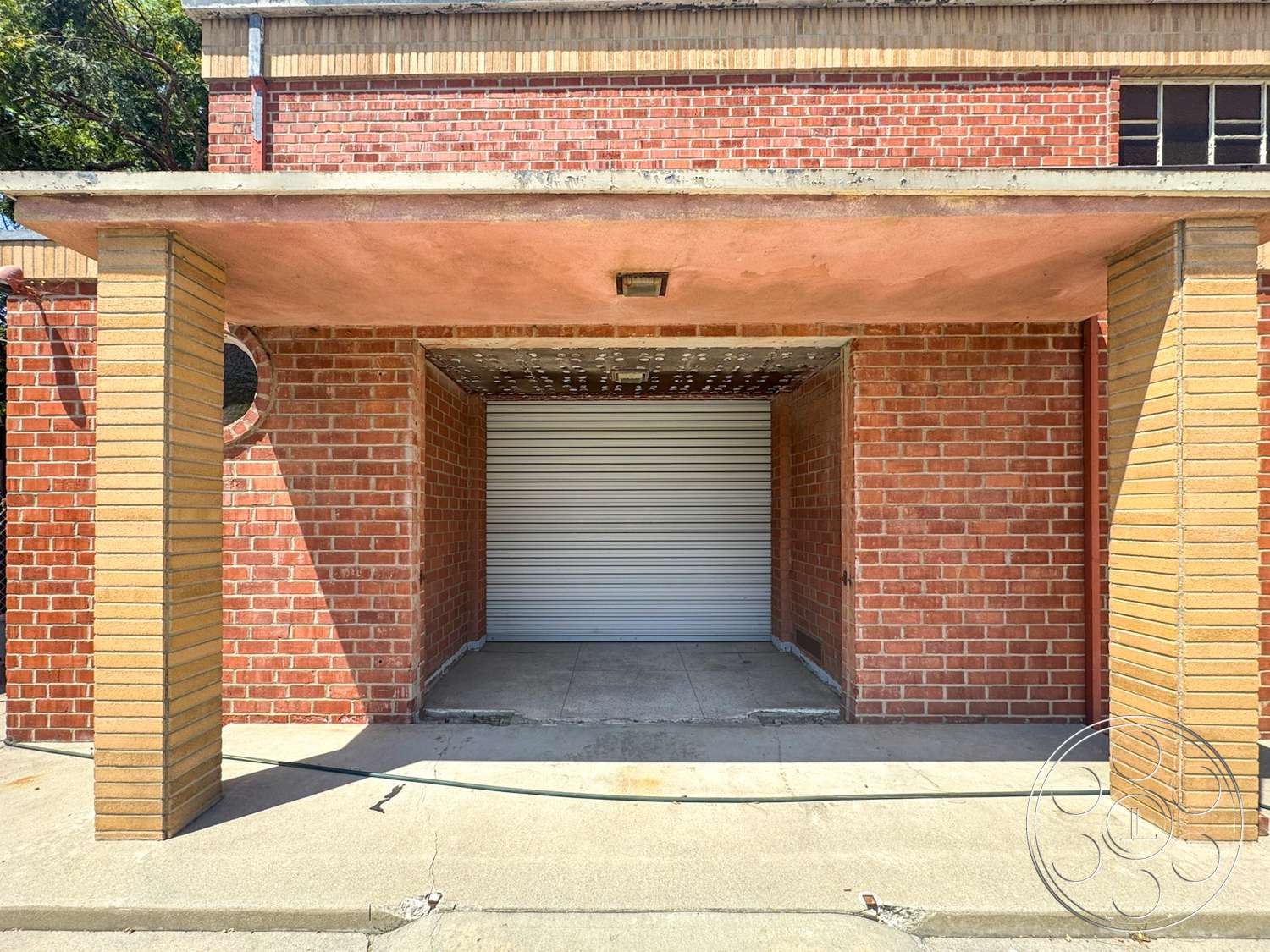 The Rosenheim Mansion - exterior, brick walls, concrete ceiling, round window feature, structural columns, concrete porch flooring, textured ceiling finish, red brick façade, yellow brick column bases, metal roll-up door, flush eaves