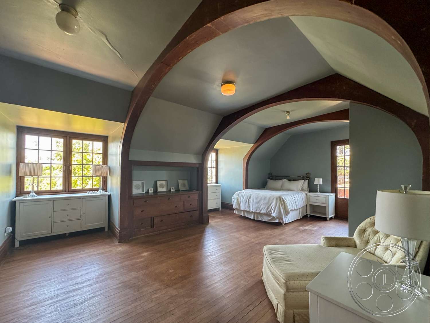 The Rosenheim Mansion - exposed wooden beams, soft white bedding, natural light from windows, queen-sized bed, hardwood bedroom floors, white painted walls, traditional interior design, view of surrounding greenery, arched ceiling structure, dual-paned windows, traditional nightstand, built-in wooden dresser, plush accent chair, task lamp on nightstand