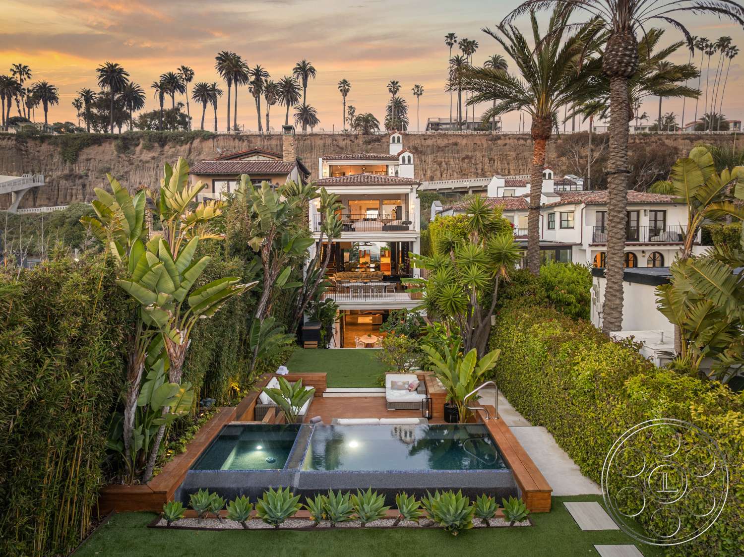 Beach 137 - exterior, grass lawn, horizontal wood fencing, terracotta tile roof, concrete pool deck, rectangular pool, stone retaining wall, bamboo privacy screen, lush palm trees, stucco home exterior, glass balcony railings, wood deck seating area, plant landscaping