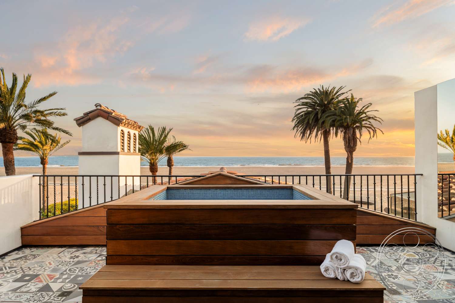 Beach 137 - exterior, white stucco walls, metal railing, Mediterranean architectural style, palm trees in landscape, textured tile patio flooring, rectangular hot tub, wood deck surrounding spa, decorative patterned tiles, sunset beach view, brick chimney with terracotta roof