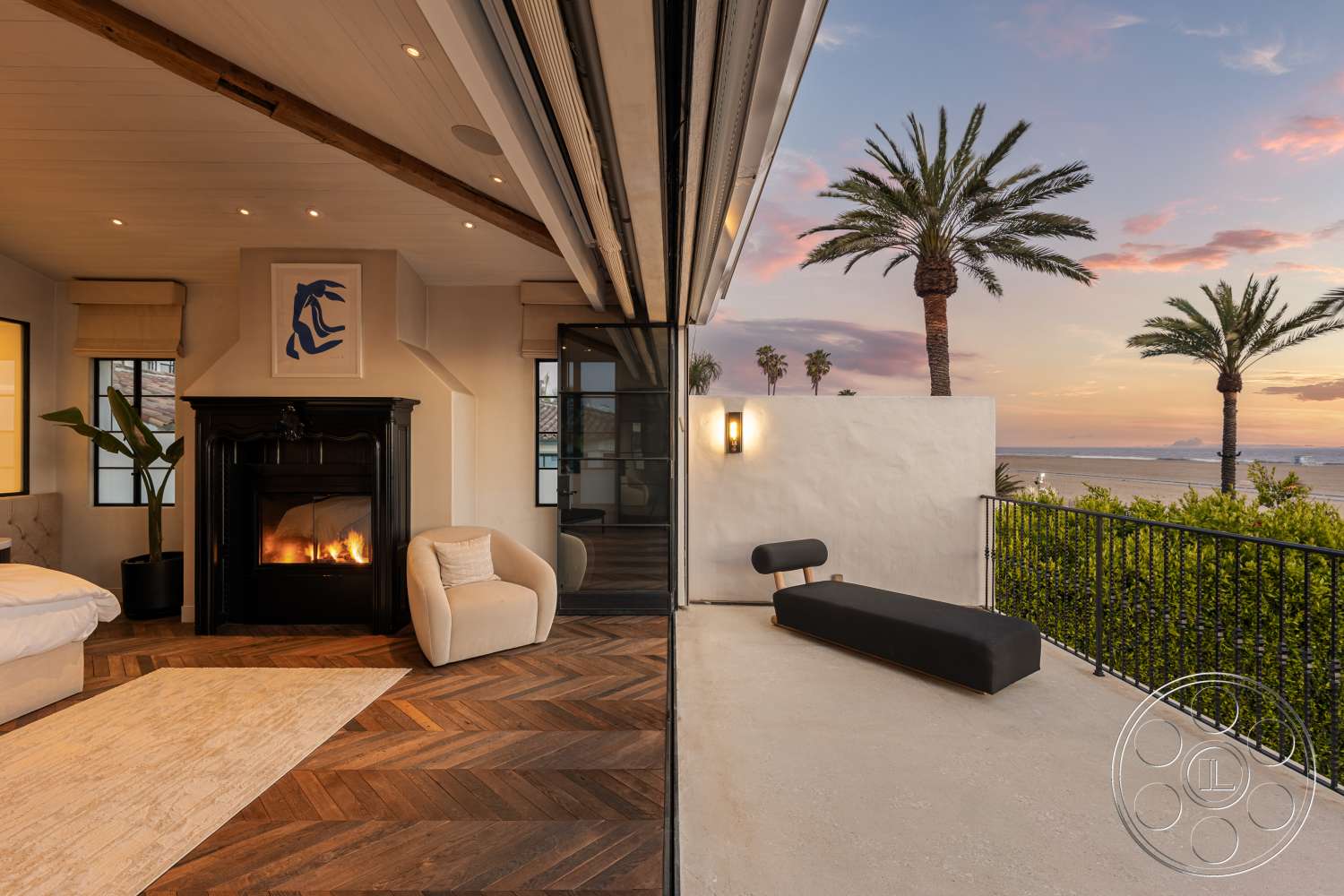 Beach 137 - neutral color palette, decorative wall art, curved lounge chair, exposed wood ceiling beams, modern minimalist aesthetic, natural light through large windows, textured plaster wall treatment, floor-to-ceiling glass doors, black stone fireplace surround, interior living room with herringbone hardwood floors, exterior concrete terrace with ocean view, palm tree backdrop