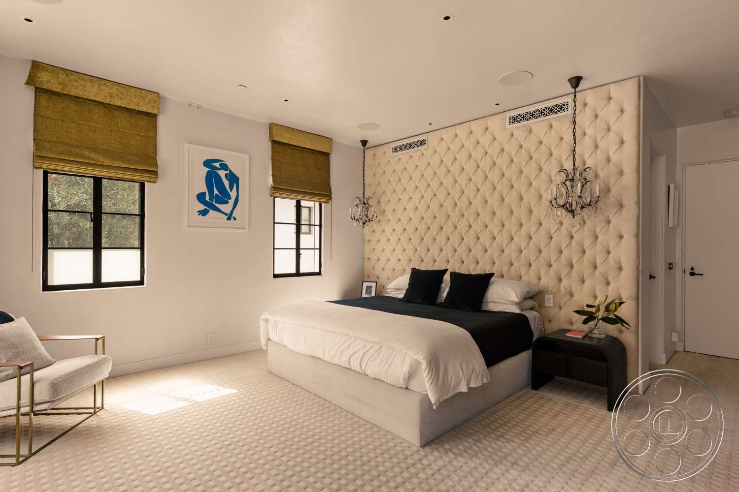 Beach 137 - neutral wall colors, framed wall art, decorative indoor plant, dark wood nightstand, hardwood bedroom floors, textured carpet flooring, modern design aesthetic, glass chandelier lighting, double-pane windows, upholstered headboard wall, cream tufted wall panels, black bed linens, golden roman shades