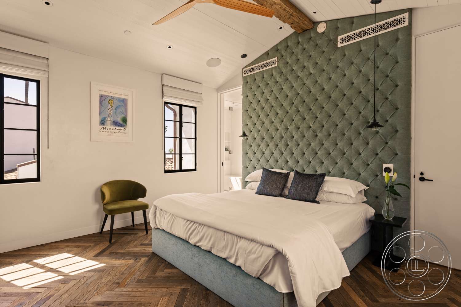 Beach 137 - floor-to-ceiling windows, black bedside table, green accent chair, white painted walls, exposed wood ceiling beam, herringbone hardwood bedroom floors, tufted green upholstered accent wall, black metal pendant lights, striped artwork on wall