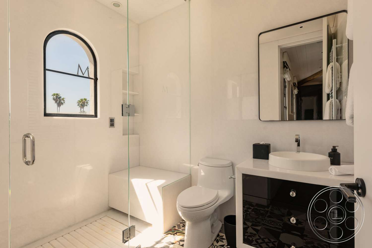 Beach 137 - glass shower enclosure, black and white color scheme, arched window, chrome faucet, rectangular bathroom mirror, modern bathroom design, white textured plaster walls, black harbor bathroom cabinetry, round white vessel sink, monochrome patterned tile flooring, floor-to-ceiling glass shower walls