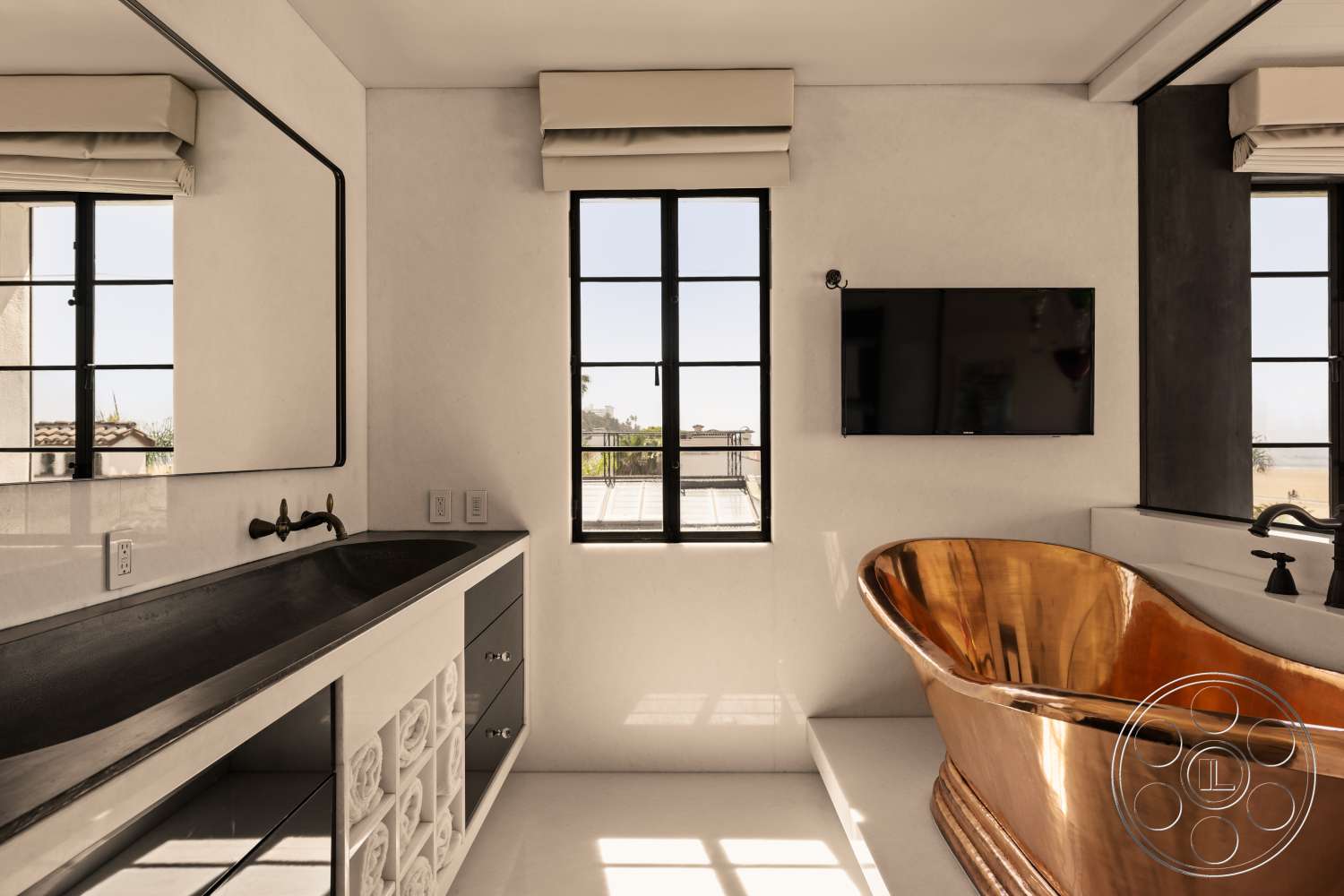 Beach 137 - black metal window frames, minimalist design aesthetic, concrete bathroom flooring, natural light from floor-to-ceiling windows, large rectangular mirror, brushed brass faucet fixtures, exposed plaster walls, freestanding copper bathtub, black concrete vanity top, chrome wall-mounted television, custom cabinetry with decorative accents