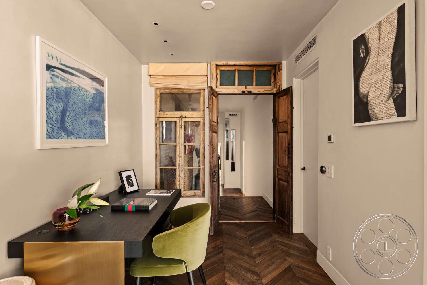 Beach 137 - decorative indoor plant, framed art on walls, wooden door frame, white painted walls, herringbone hardwood flooring, exposed wood details, transom window above door, dark wooden desk, green velvet chair