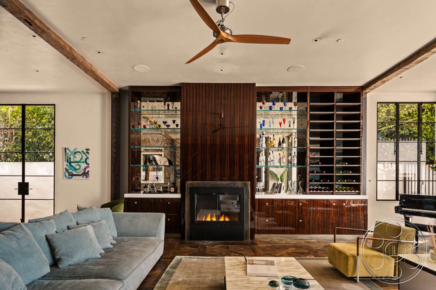 Beach 137 - open floor plan, glass windows, glass shelving, marble countertop, geometric area rug, dark wood paneling, wood ceiling beams, plush fabric sofa, contemporary living room, modern bar area, black fireplace, white painted walls, exposed brick accent wall, colorful accent chairs