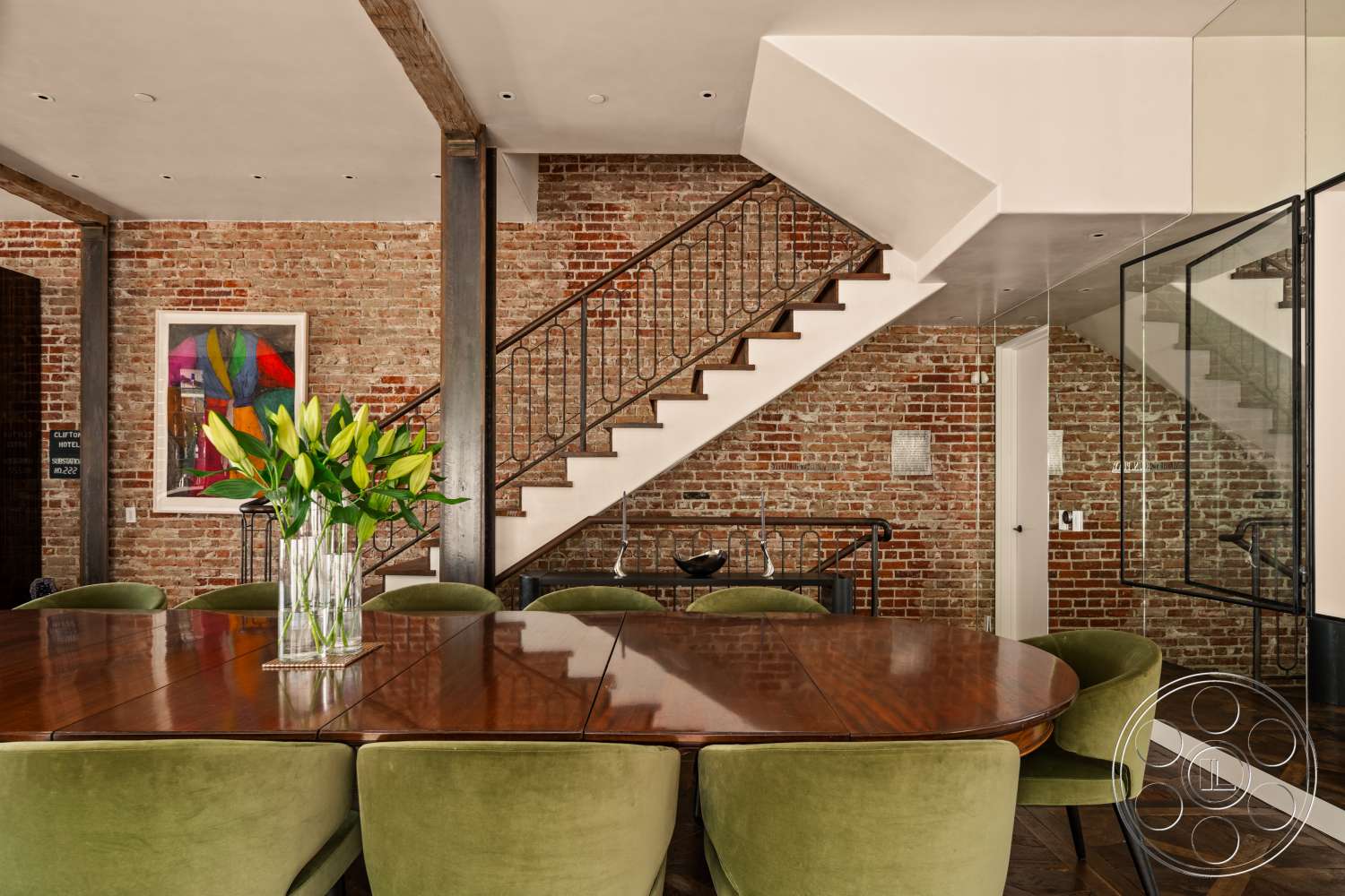 Beach 137 - floating staircase, wall-mounted artwork, glass partition walls, wood beam ceiling, oval dining table, exposed brick accent wall, steel stair railings, hardwood dining room floors, green velvet dining chairs