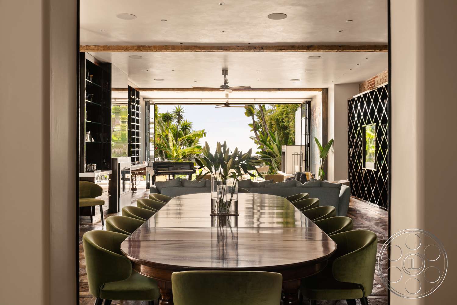 Beach 137 - concrete flooring, wood dining table, exposed wood ceiling beams, large windows with garden view, floor-to-ceiling glass doors, tropical plant decor, green velvet dining chairs, black accent wall with diamond pattern, modern shelf system