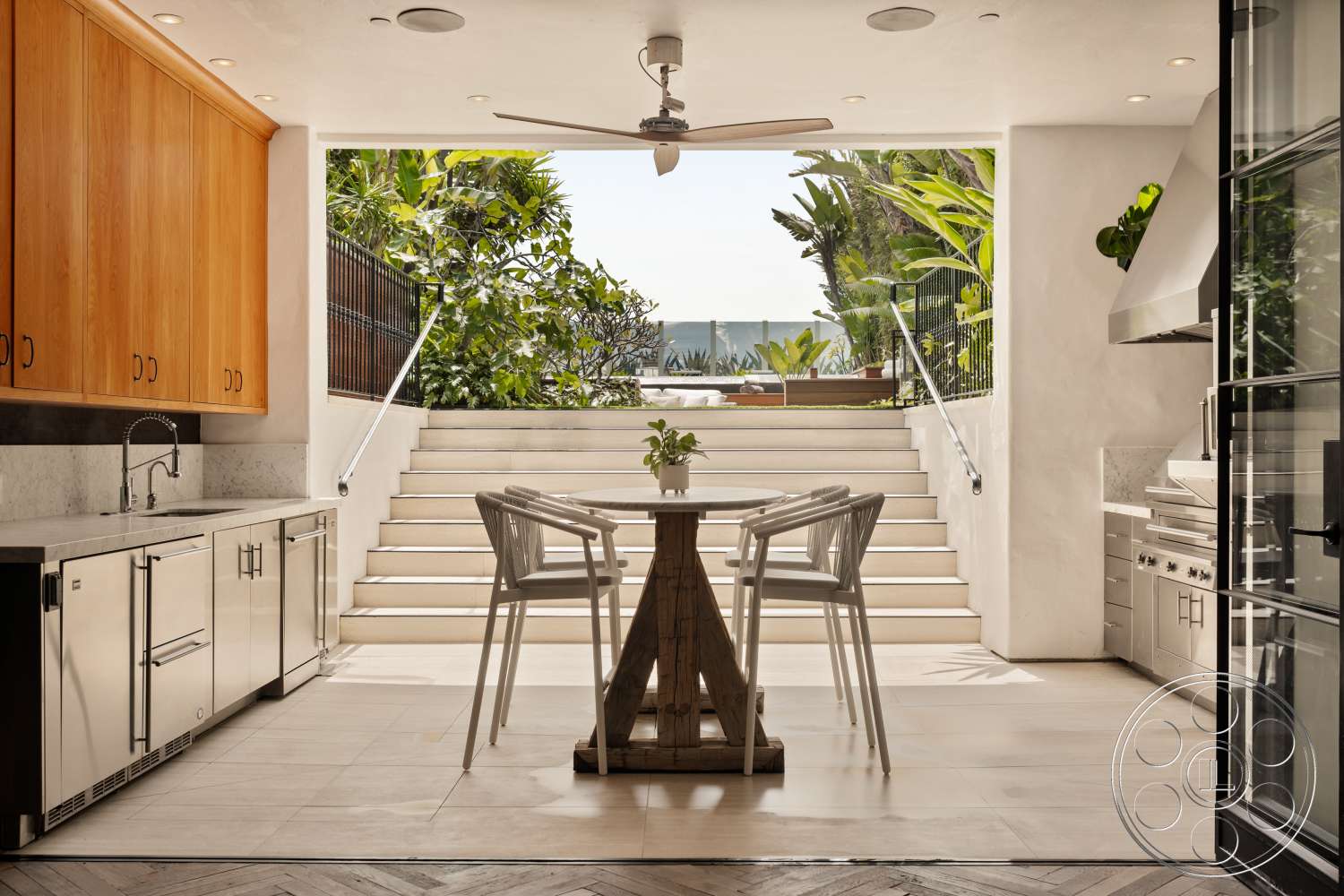 Beach 137 - stainless steel appliances, natural wood cabinetry, concrete stairs, herringbone pattern flooring, white marble countertop, contemporary bar stools, stainless steel sink, modern dining table, recessed ceiling lights, light tile flooring, open concept kitchen, minimalist kitchen design, outdoor view with greenery, floor-to-ceiling sliding glass doors, garden patio access