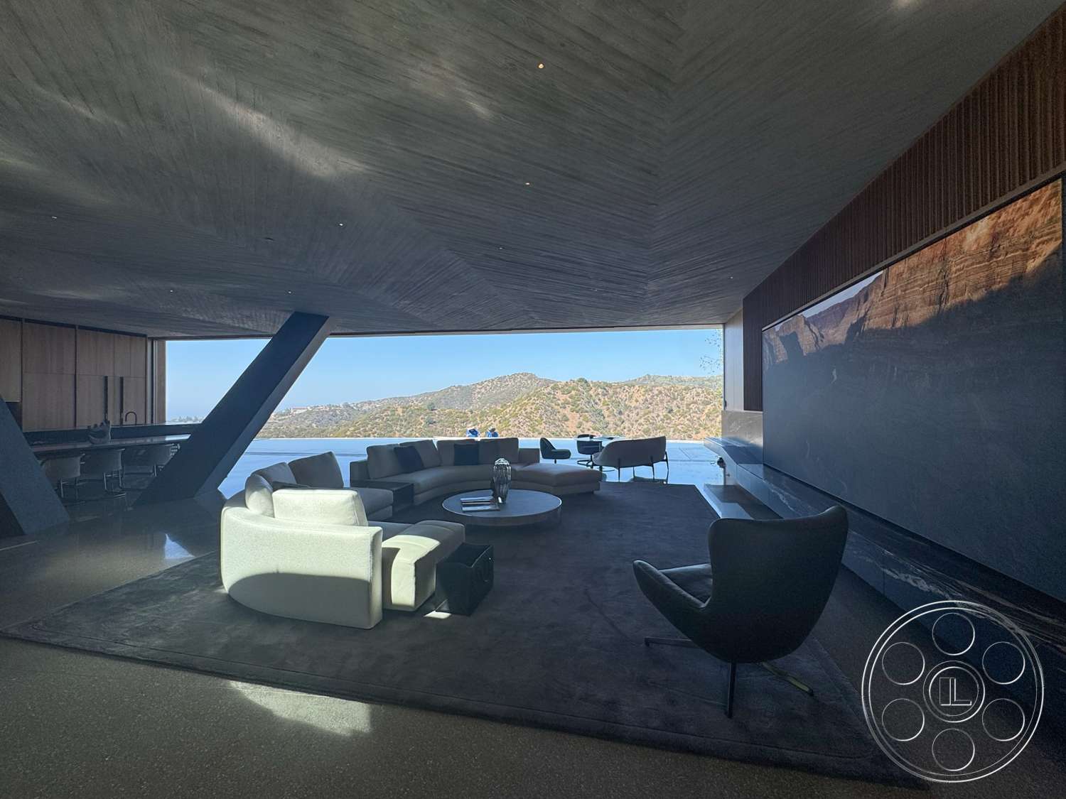Modern 516 - round coffee table, concrete flooring, minimalist design elements, open concept layout, floor-to-ceiling windows, exposed concrete ceiling, plush area rug, black armchair, modern sectional sofa, panoramic mountain view, dark hardwood accent wall