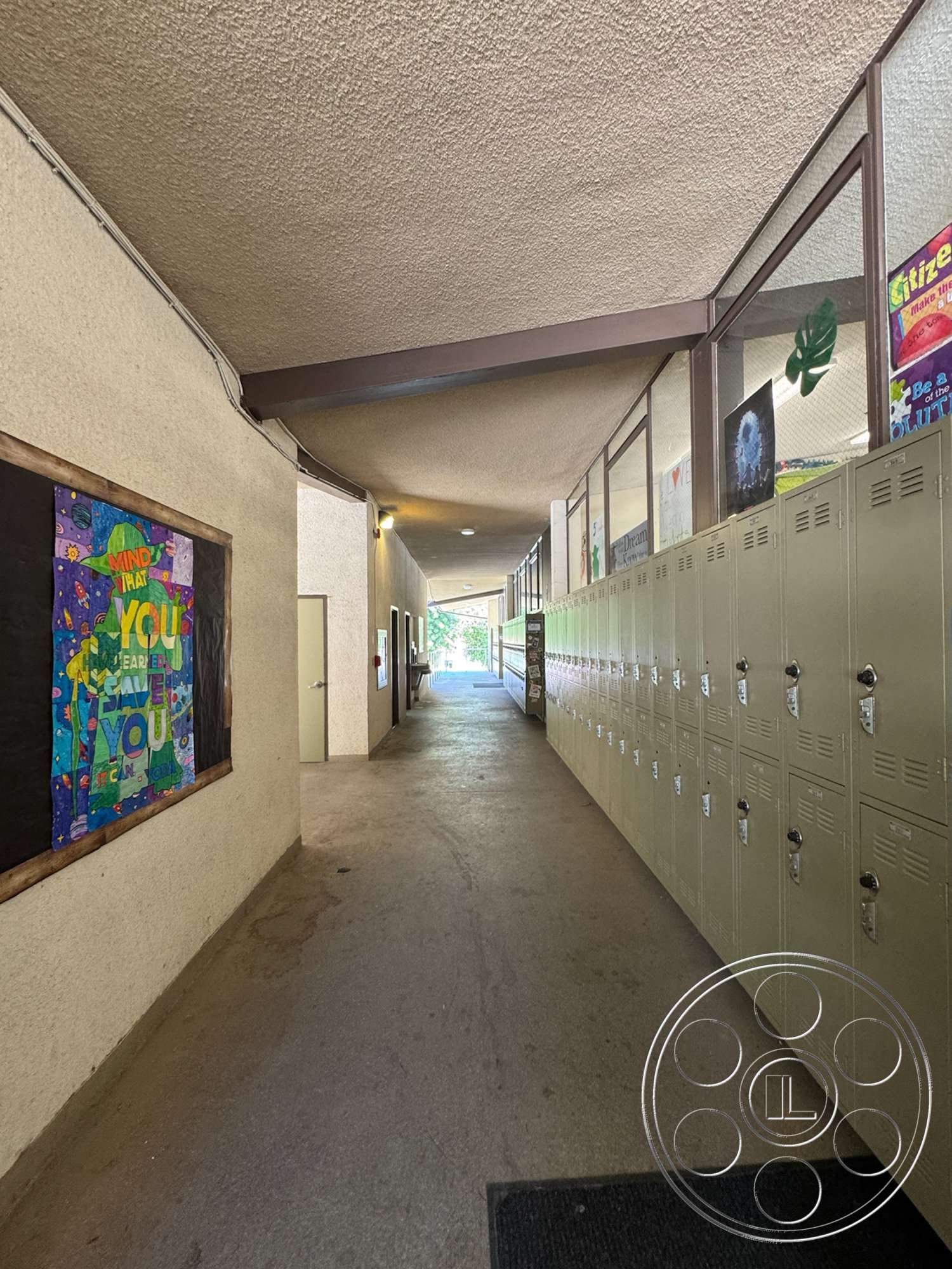 School 20 - concrete flooring, textured plaster walls, metal lockers, glass partition walls, interior corridor, industrial ceiling beams, wooden bulletin boards, rectangular ceiling light fixtures, natural light from entrance, student artwork displays