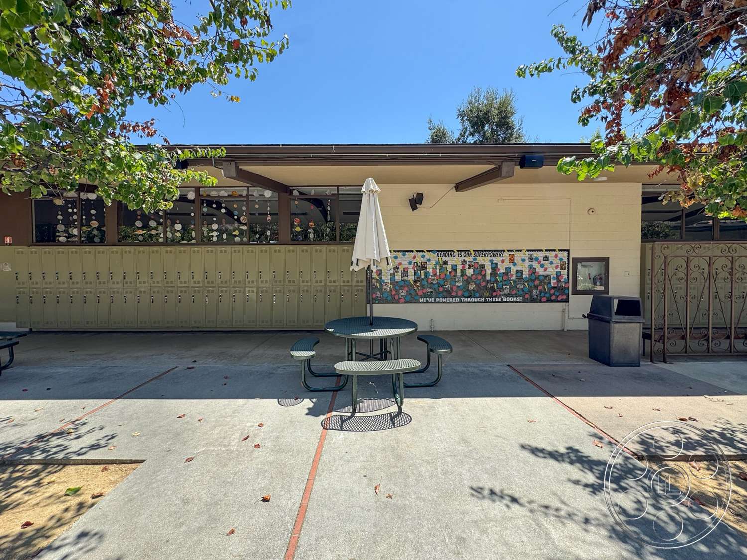 School 20 - exterior, landscaped surroundings, textured plaster walls, metal benches, concrete patio floor, decorative mural wall, sunlit open space, metal picnic table, green locker walls, awning shade umbrella