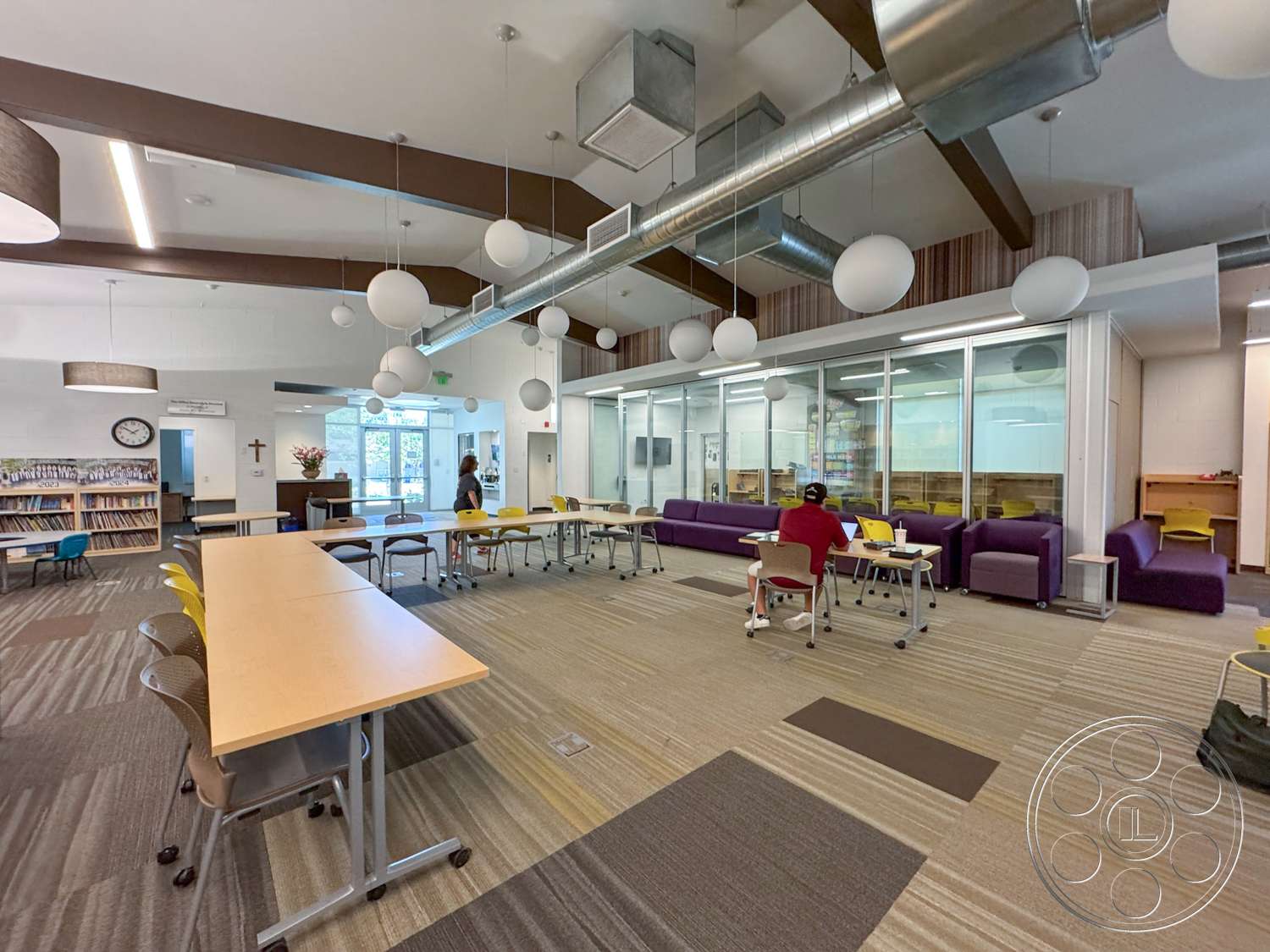 School 20 - accessibility features, pendant lighting fixtures, ergonomic chairs, recessed ceiling lighting, natural light through large windows, exposed wood beam ceiling, glass partition wall, open layout space, carpet tile flooring, modular classroom tables, modern educational design, library shelving units, vertical wood panel wall treatment, purple lounge seating, collaborative study area, community activity space