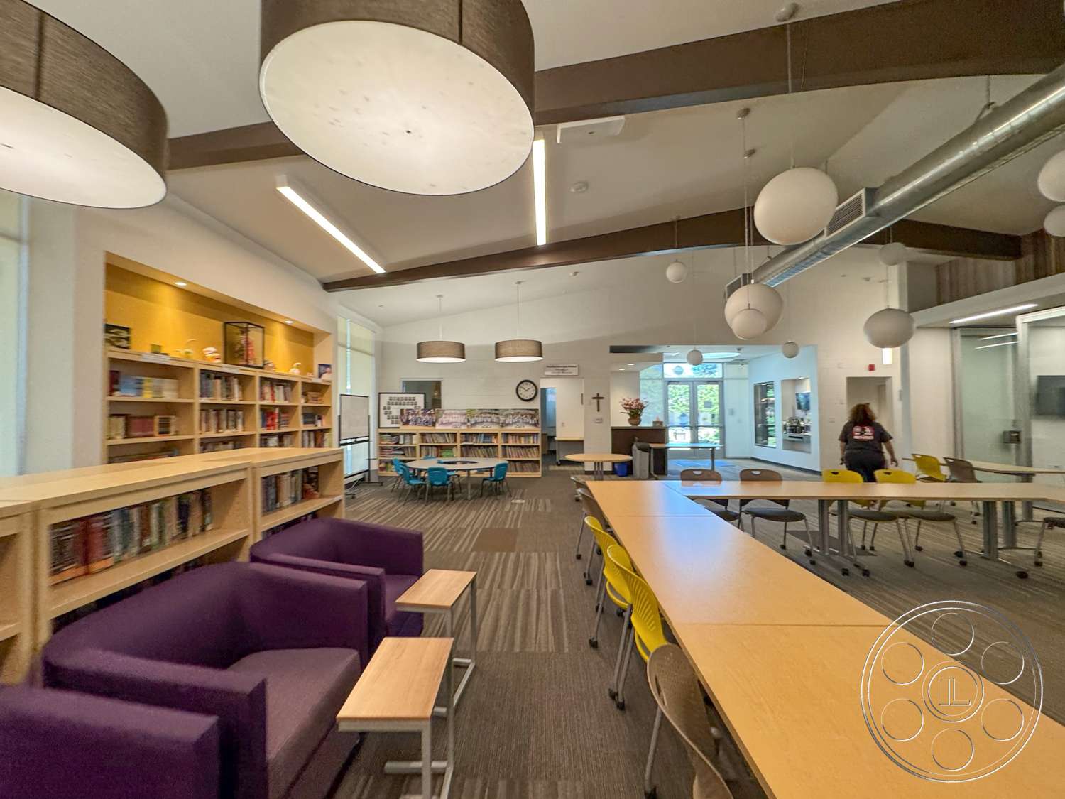 School 20 - modern pendant lighting, floor-to-ceiling windows, textured wall panels, carpet flooring, built-in bookshelves, wood beam ceiling, exposed metal ductwork, rectangular study tables, purple lounge chairs, yellow plastic chairs, reading nook area, open study space, community library setting