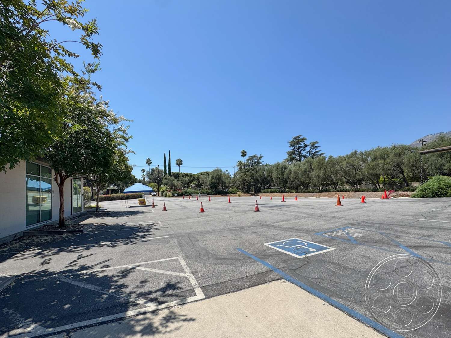 School 20 - exterior, green foliage, asphalt parking lot, surrounding palm trees, landscaped garden area, commercial building façade, decorative traffic cones, visible blue sky, waiting area with tent, concrete access path