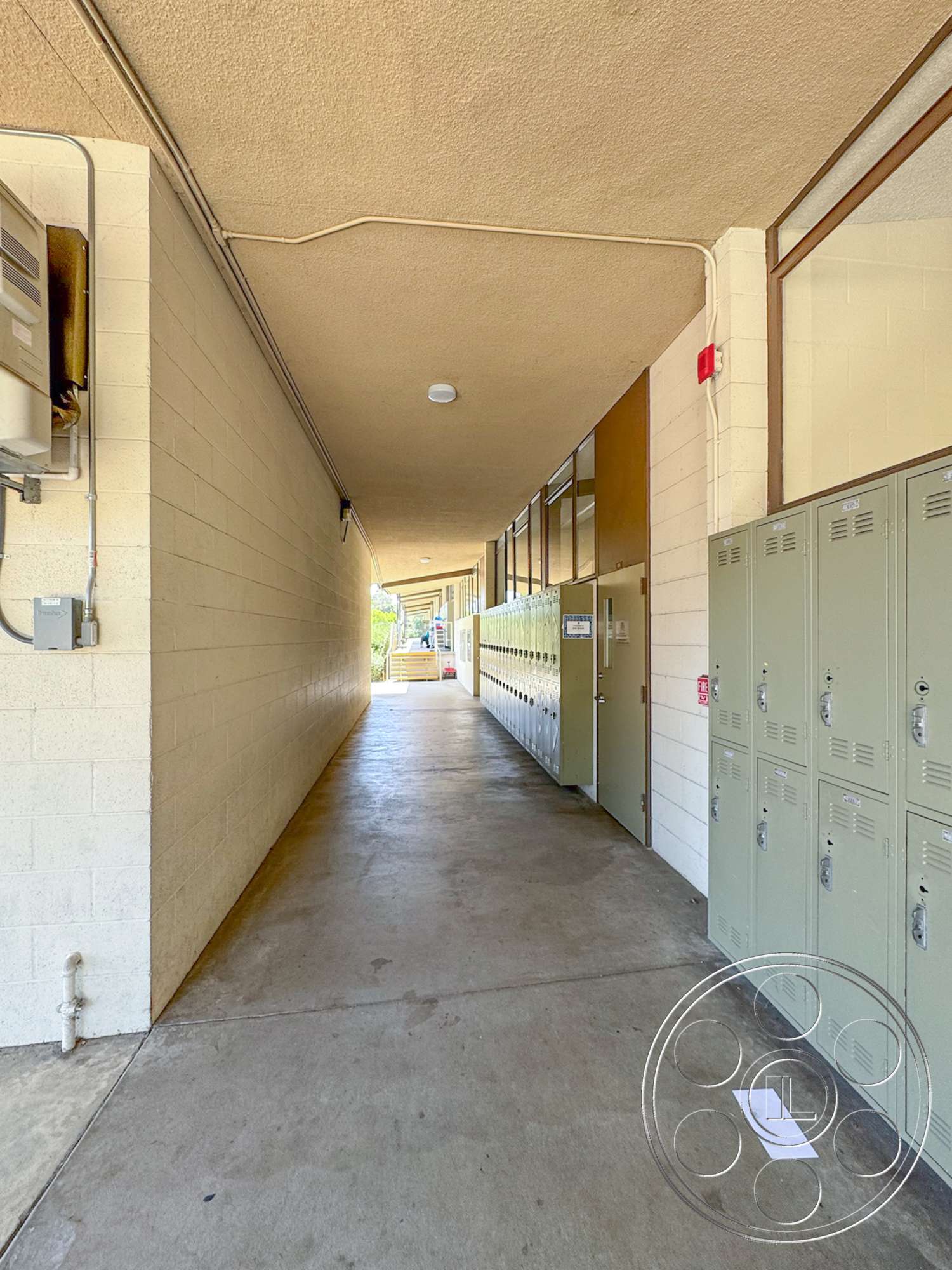 School 20 - exterior, glass windows, metal lockers, concrete corridor flooring, cinder block walls, drop ceiling with flush lights, painted wall surfaces, school hallway setting