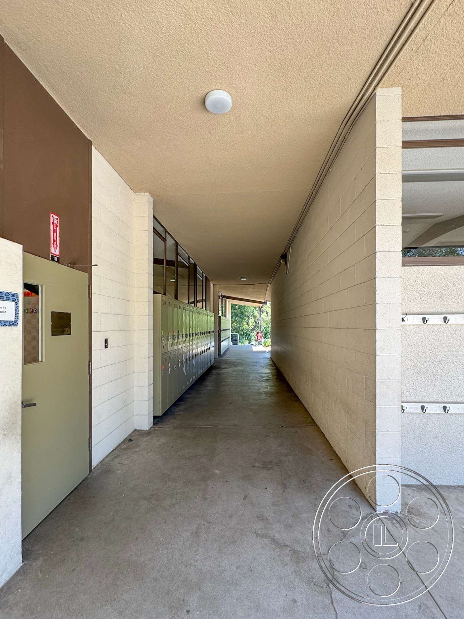 School 20 - concrete block walls, flat ceiling, concrete walkway, textured plaster wall, exterior hallway, straight corridor, green lockers, lockers mounted on wall, fluorescent ceiling light fixture, double-leaf door