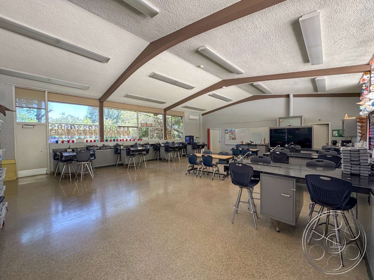School 20 - neutral wall colors, textured plaster ceiling, large floor-to-ceiling windows, curtained windows, whiteboard wall, rectangular classroom layout, plastic stackable chairs, vinyl classroom flooring, bright LED ceiling lights, high ceiling with exposed wood beams, metal workspace tables, organized classroom setting, educational materials display