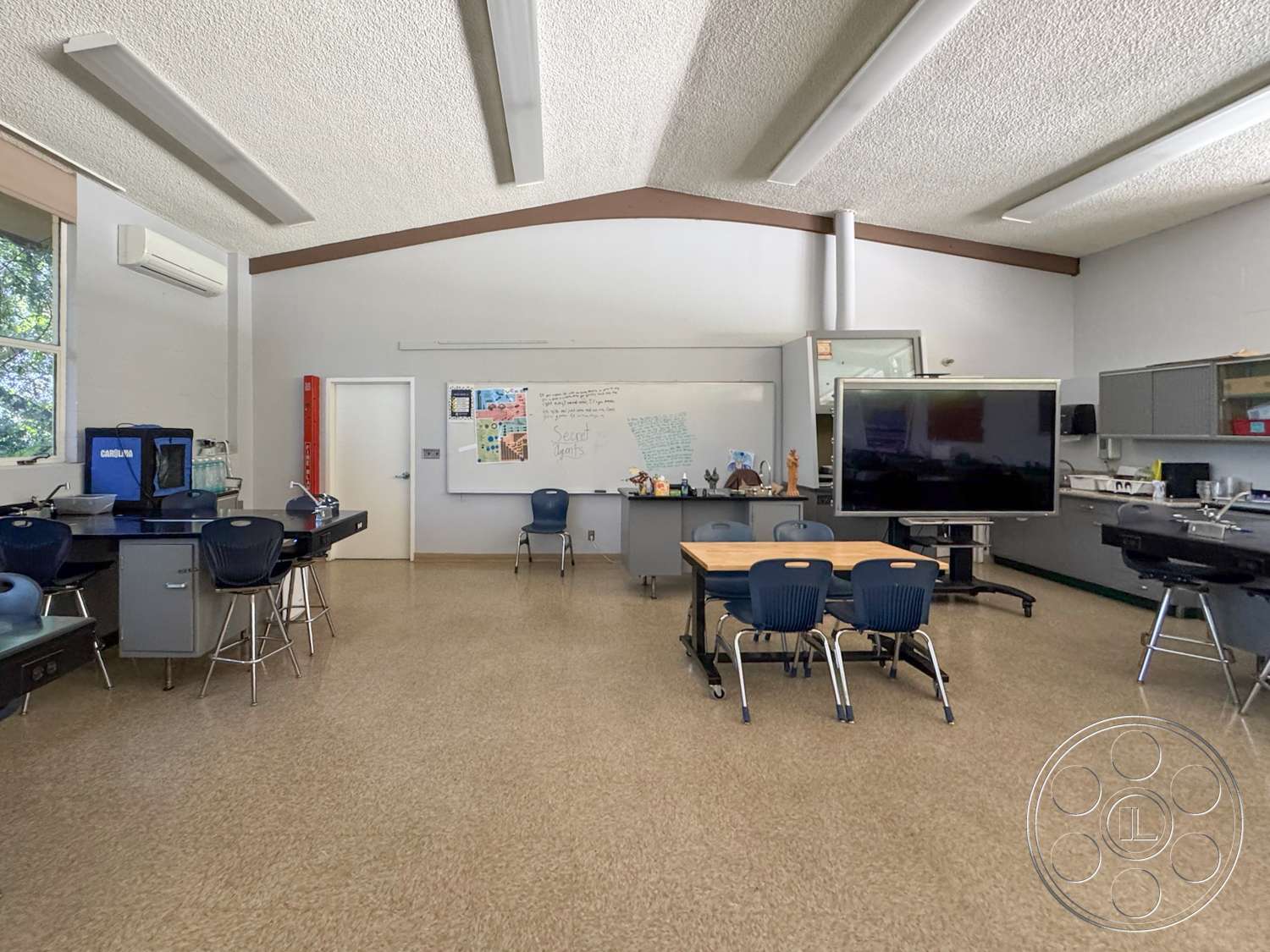 School 20 - high ceilings, large windows, multi-functional space, acoustic ceiling tiles, wood beam accents, white painted walls, wall-mounted display screen, modern classroom design, double-door entry, non-slip vinyl floor, student desk seating, educational equipment area, science lab stations, cabinets with glass fronts